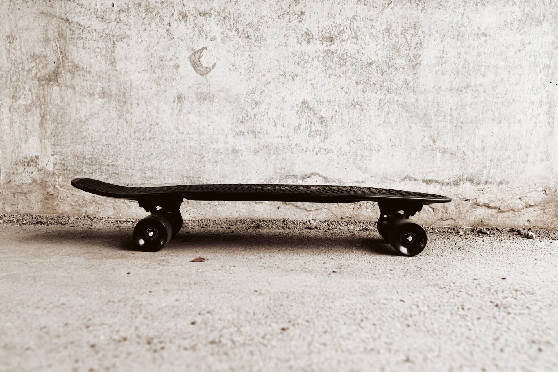 Ein Skateboard steht auf einem hellen Untergrund vor einer hellen Wand.