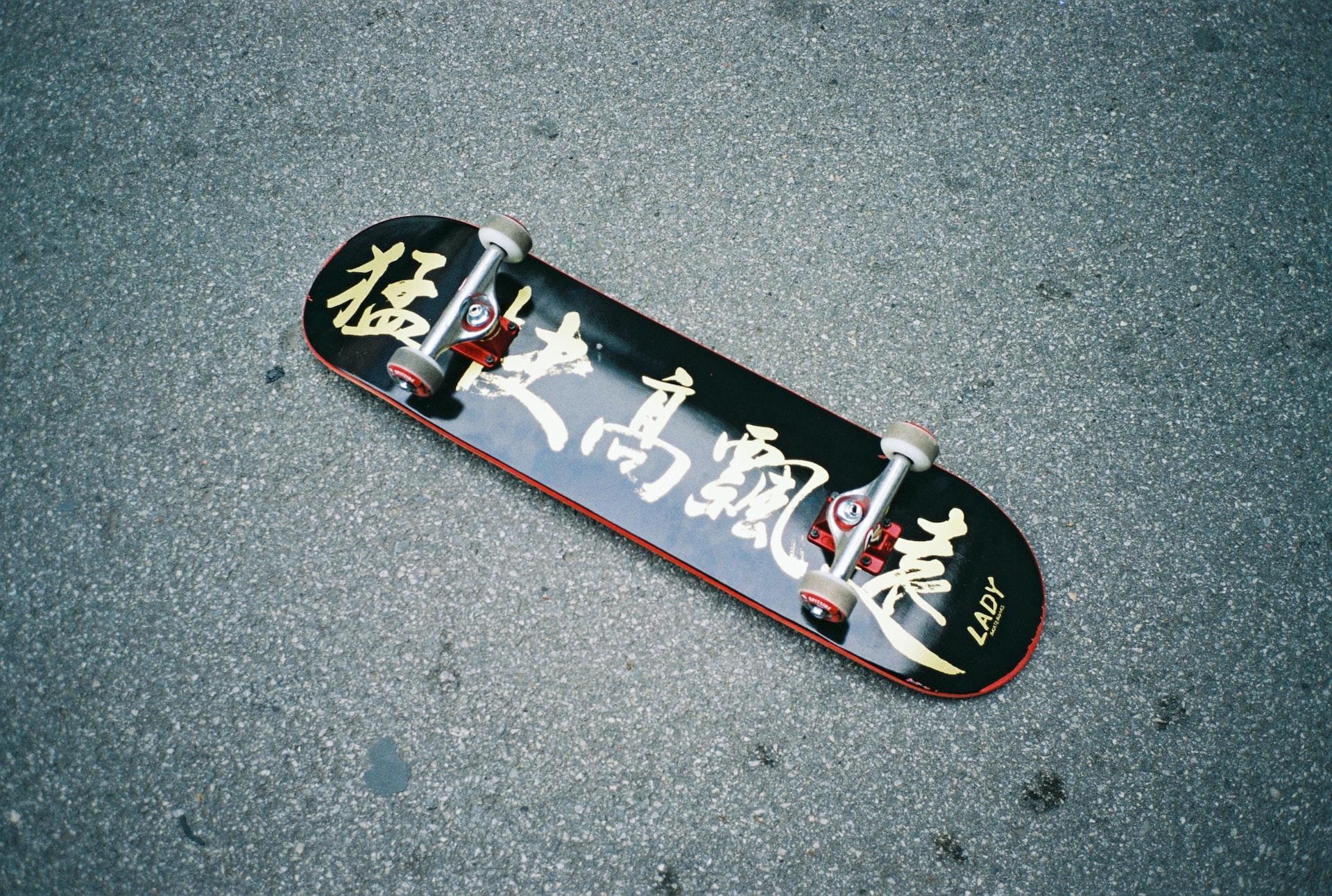 Ein Skateboard mit chinesischen Schriftzeichen liegt mit den Rollen nach oben auf dem Asphalt.