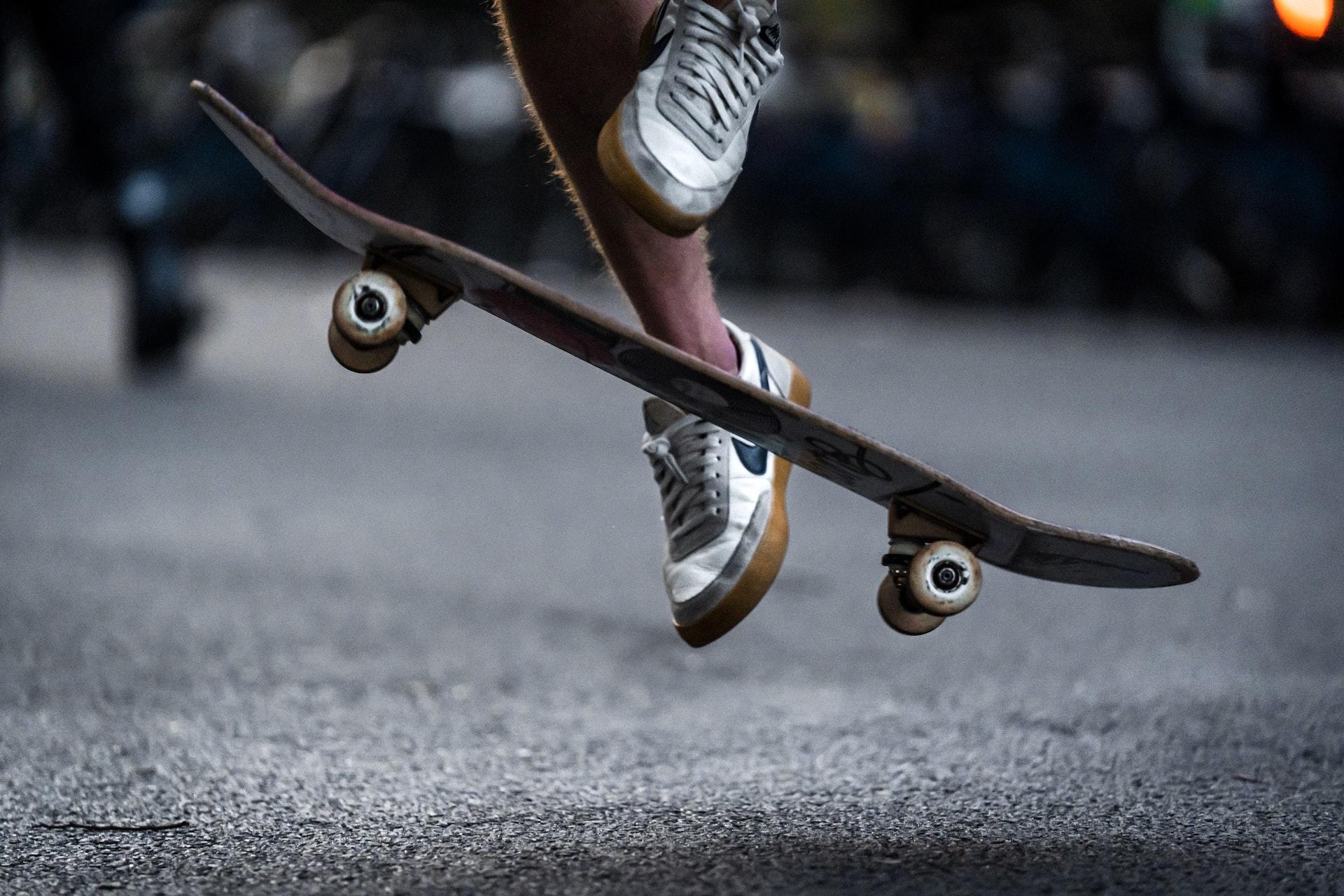 Zwei Füße in Turnschuhen sind einige Zentimeter über dem Boden und dazwischen ist ein Skateboard.