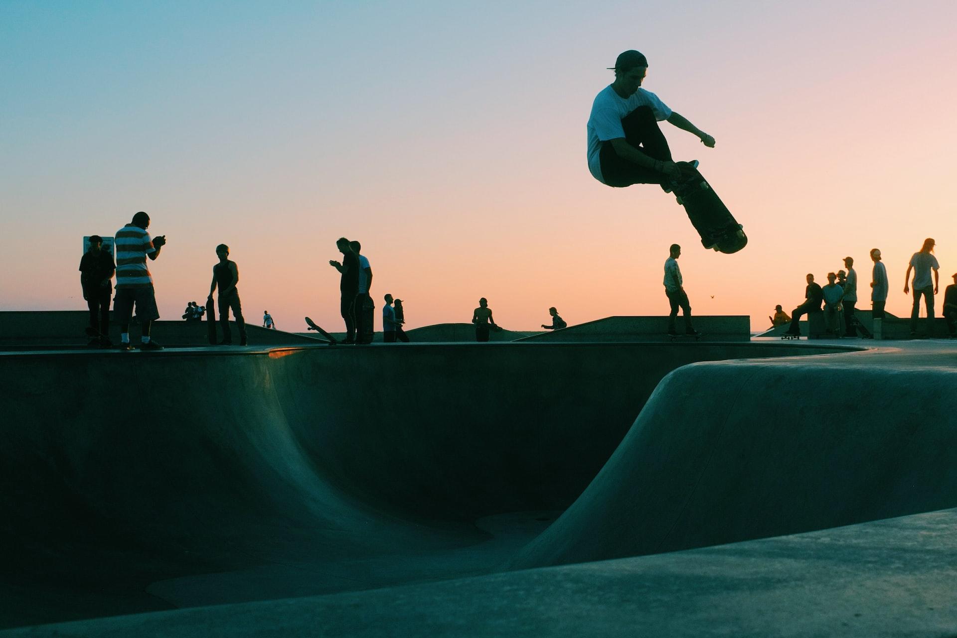 In einem Skatepark im Abendrot springt eine Person mit Skateboard in die Luft.