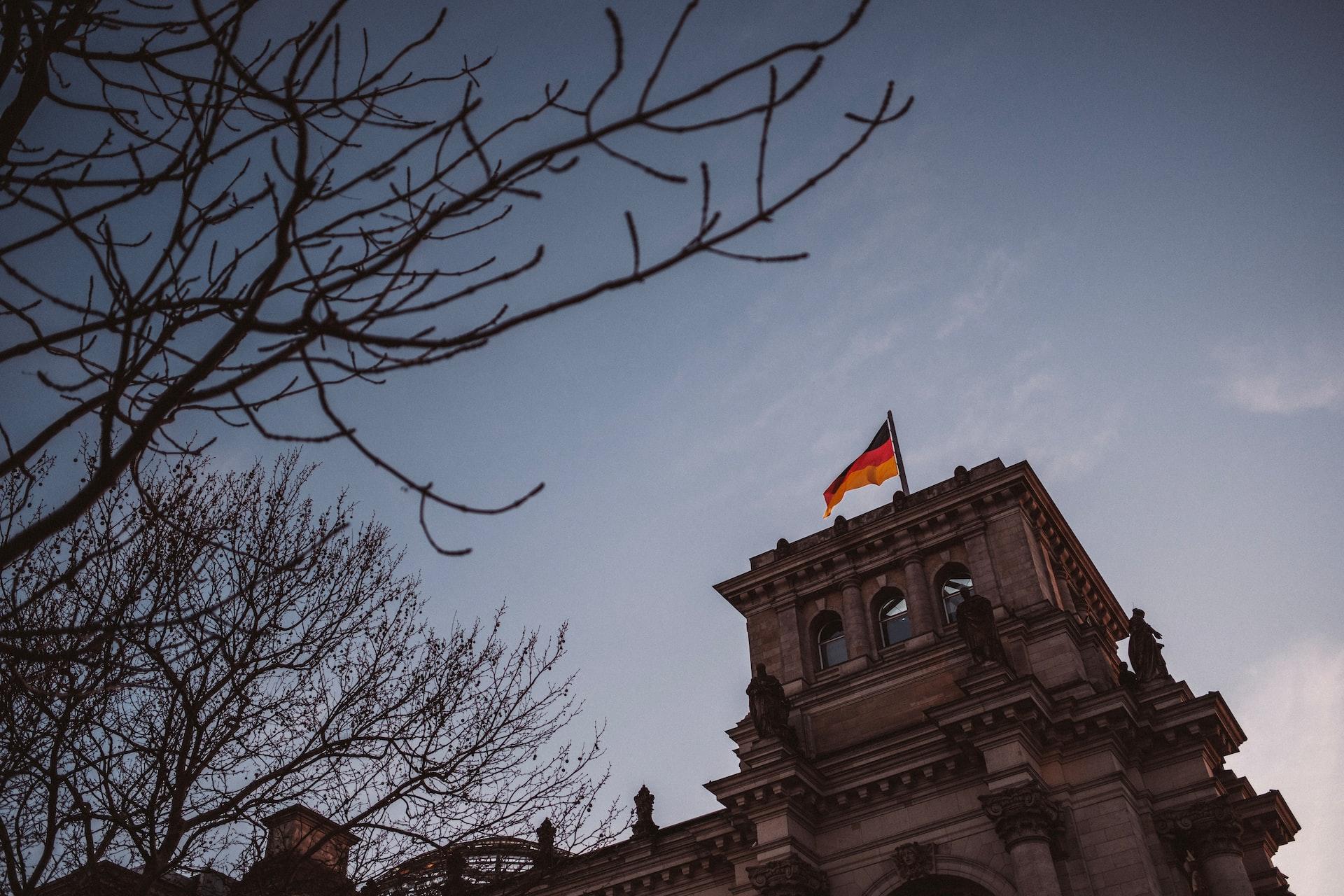 Auf einem Gebäude hinter blattlosen Ästen weht die deutsche Flagge im Wind.
