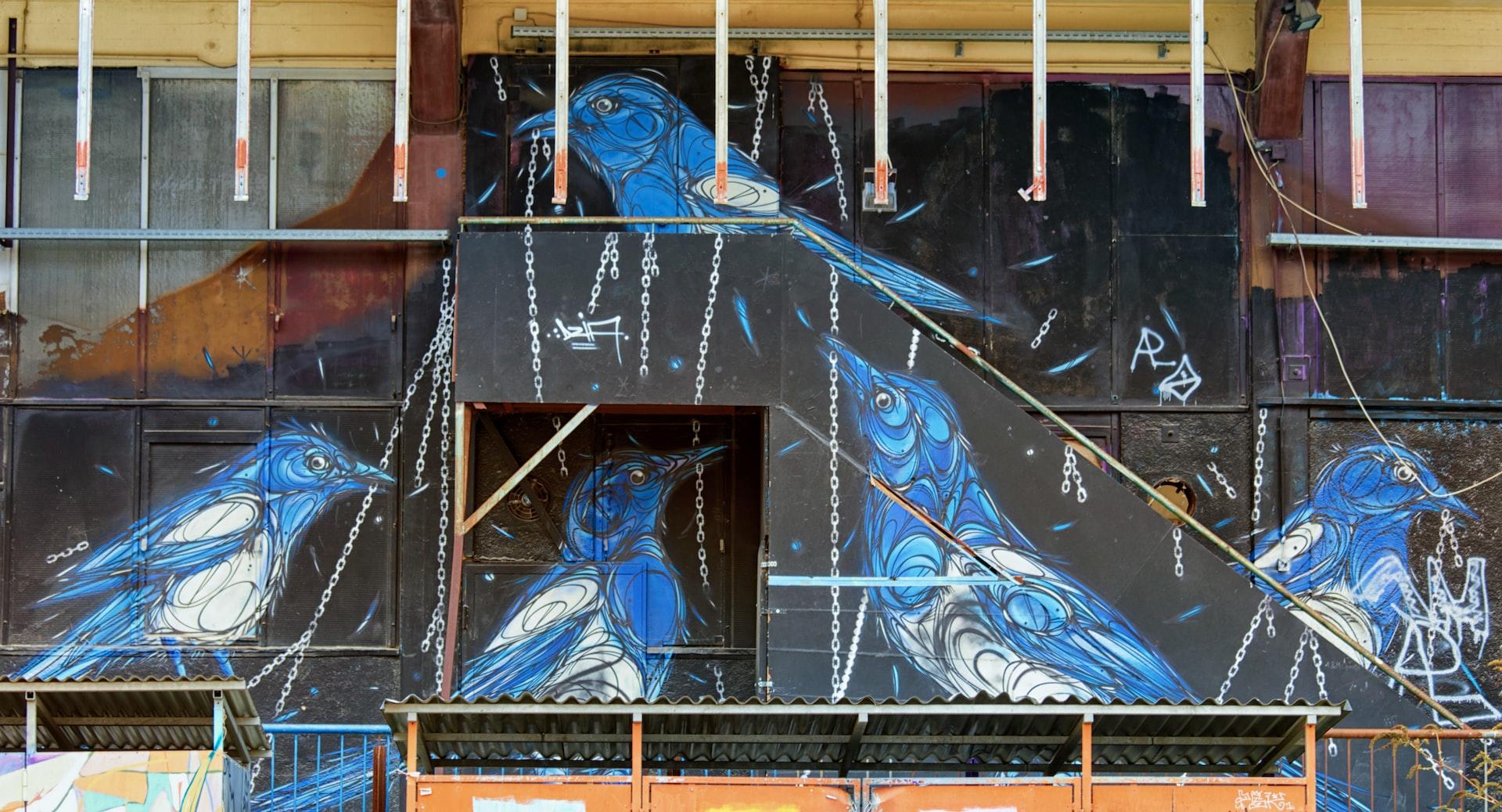 Auf die Außenwand eines alten Fabrikgebäudes sind blaue Vögel aufgemalt.