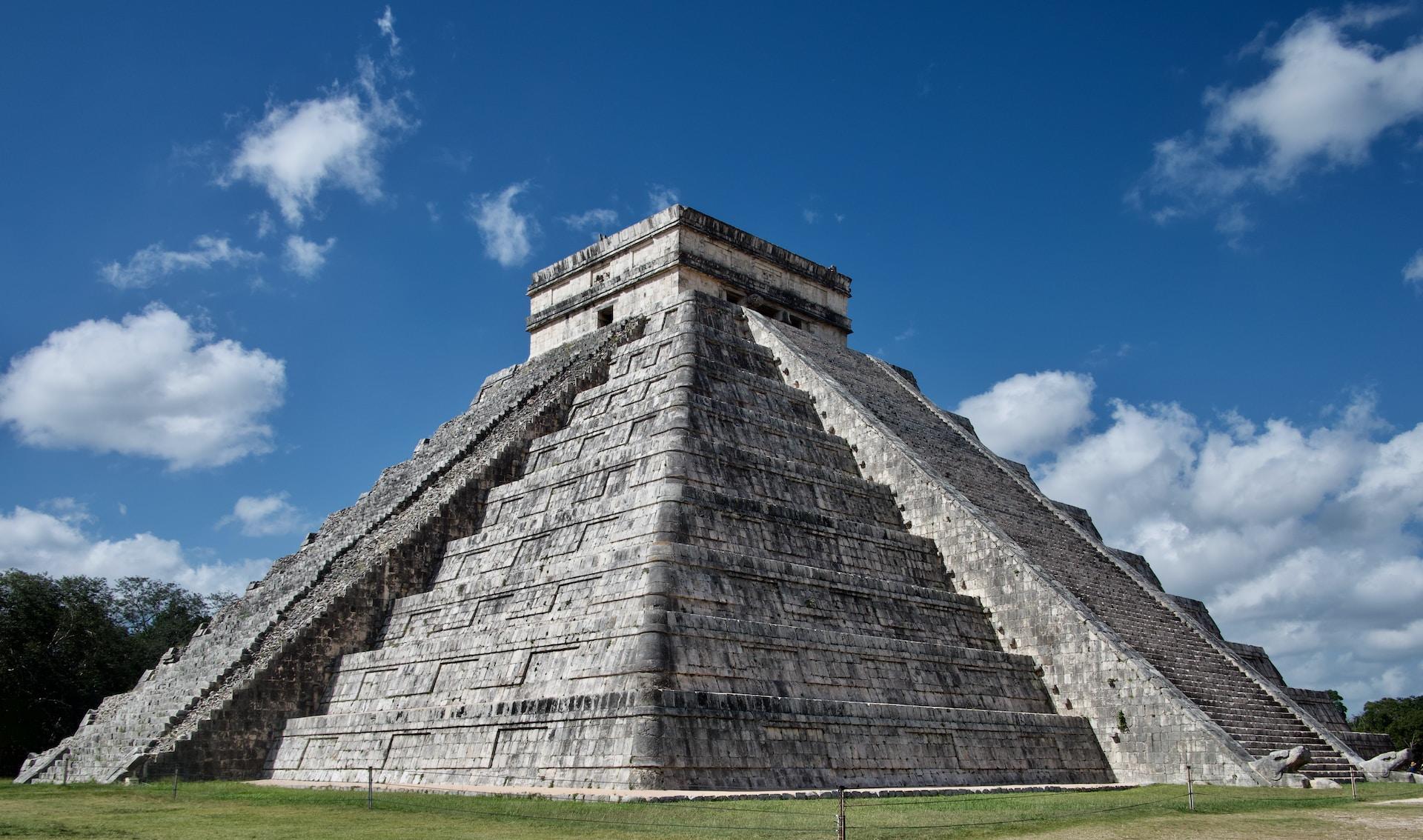 Eine in Stufen gebaute Maya-Pyramide erhebt sich in den blauen Himmel hinein.