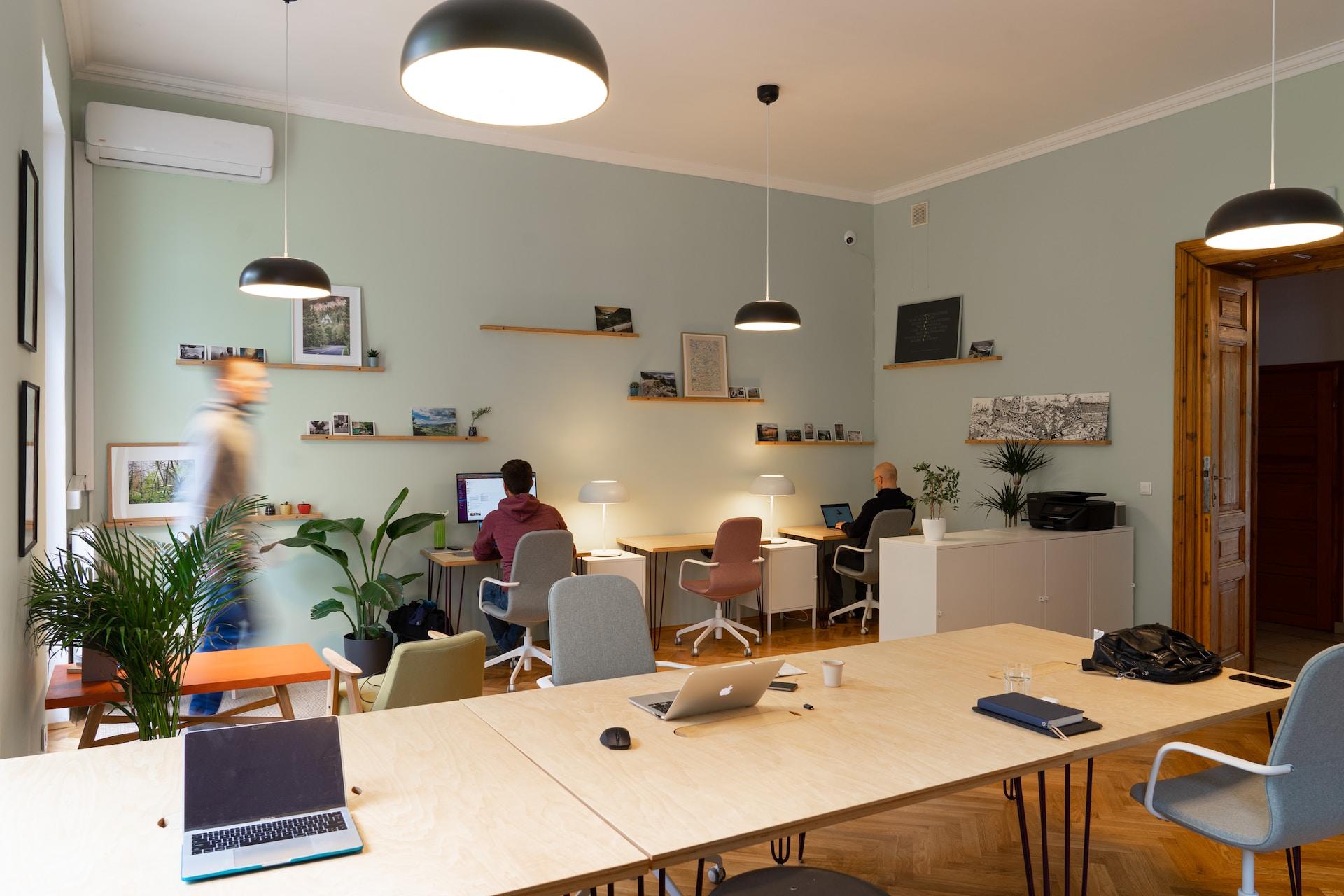 Büroraum mit langem Tisch und Laptops sowie drei Menschen.