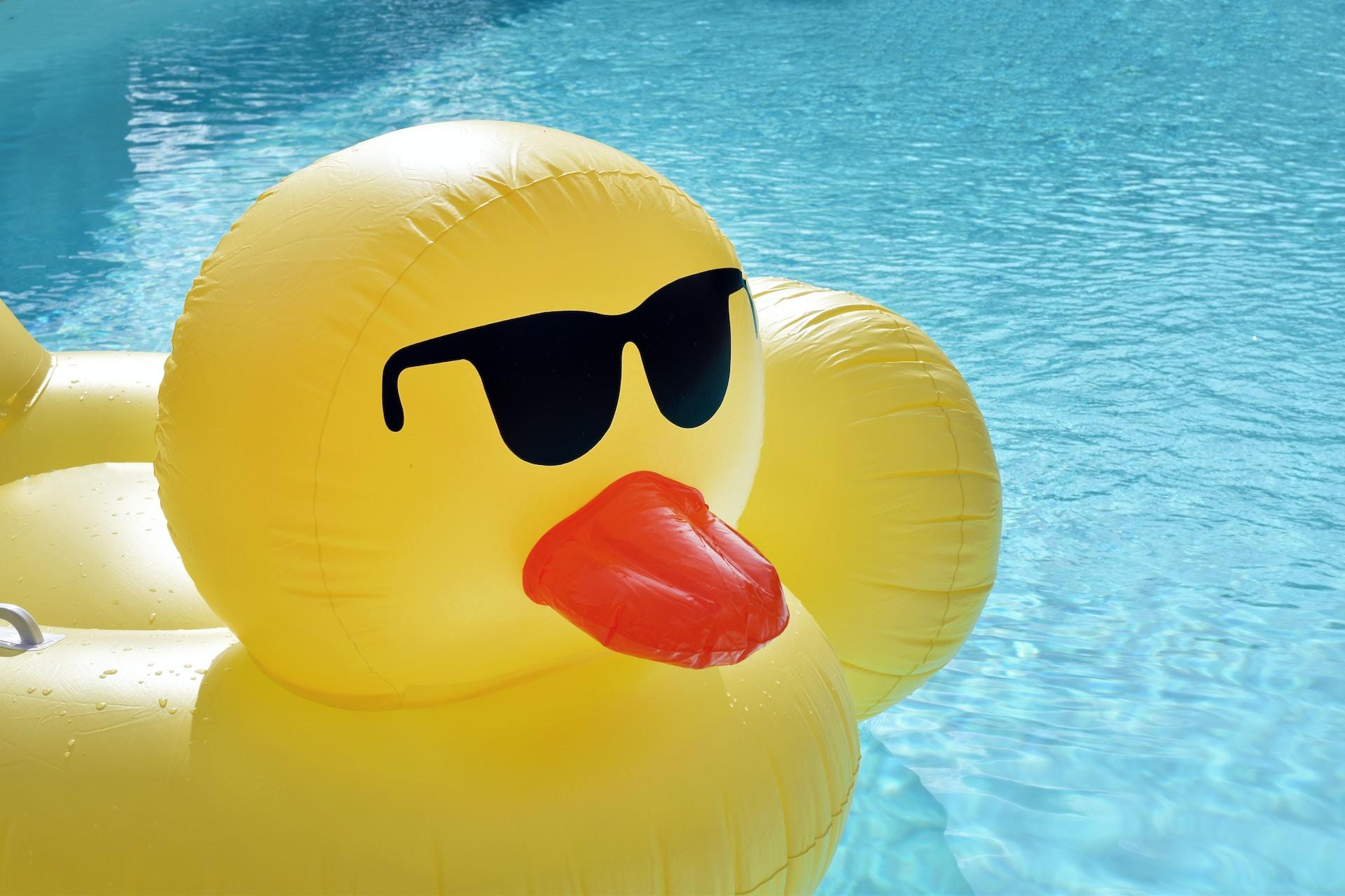 Ein Schwimmreif in Form einer Ente mit Sonnenbrille schwimmt auf dem Wasser.