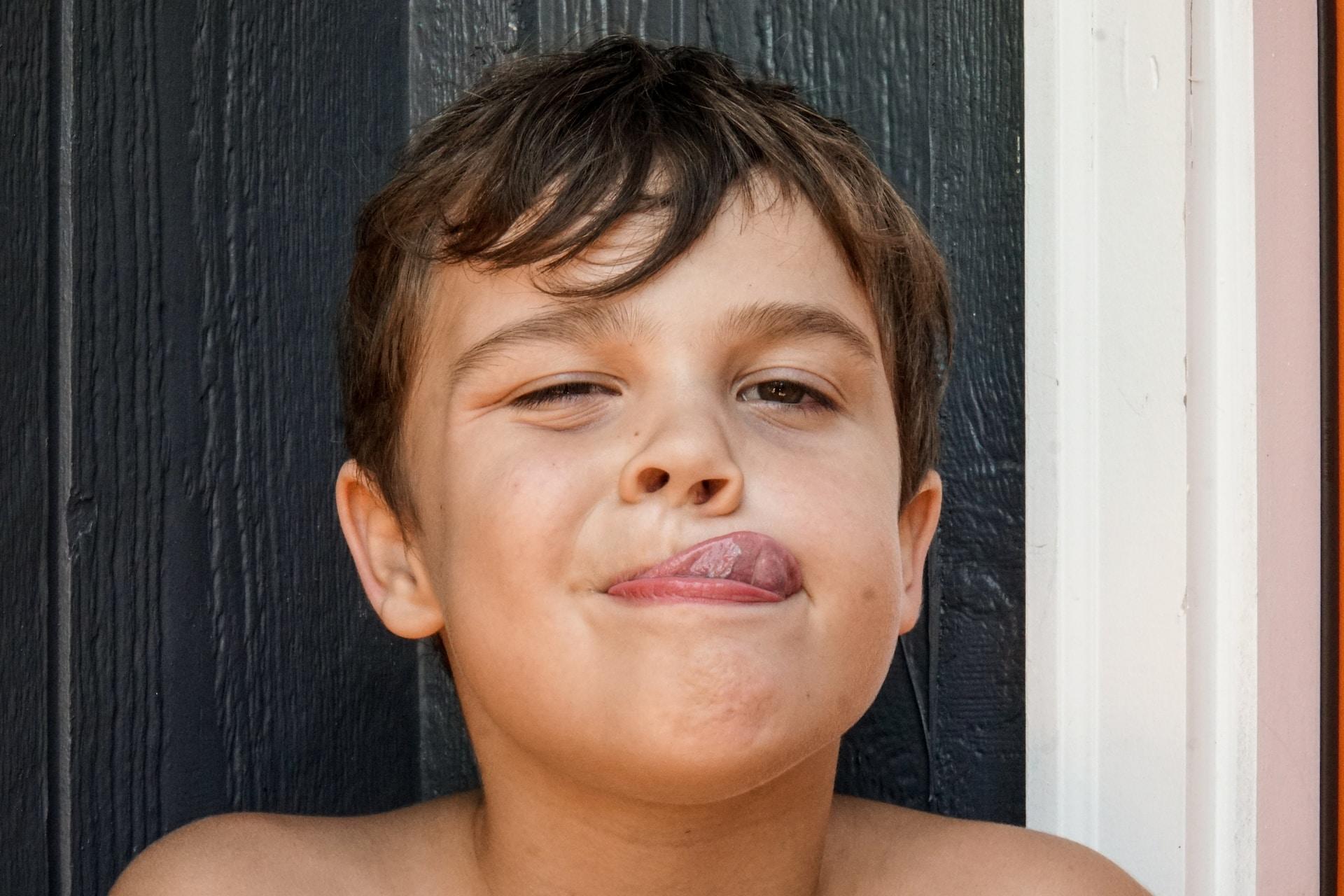Ein Kind streckt die Zunge zwischen den Lippen durch und hat ein Auge halb geschlossen.