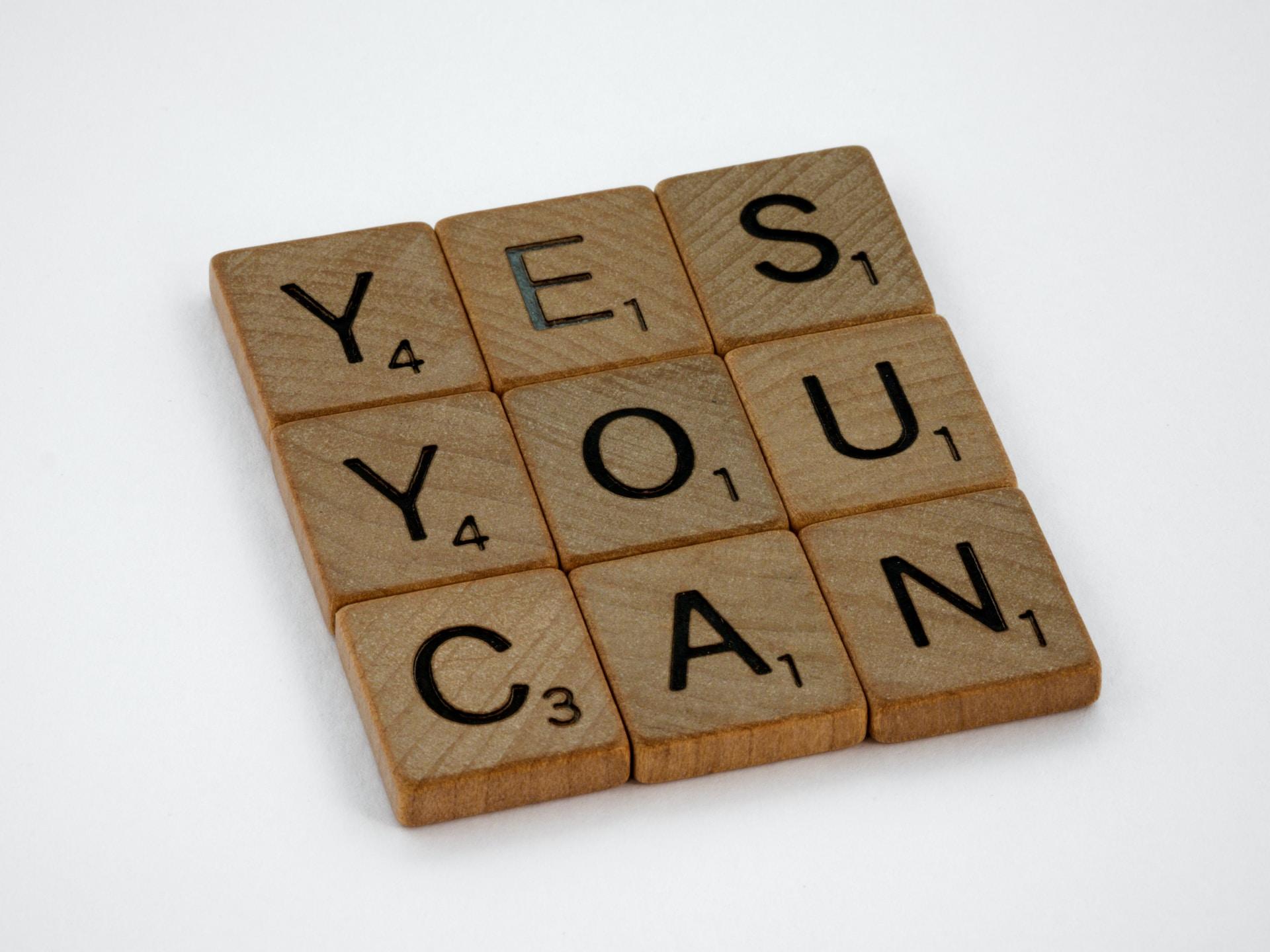 Neun Holzblöcke mit Buchstaben sind zu einem Viereck angeordnet und bilden den Text "Yes you can".