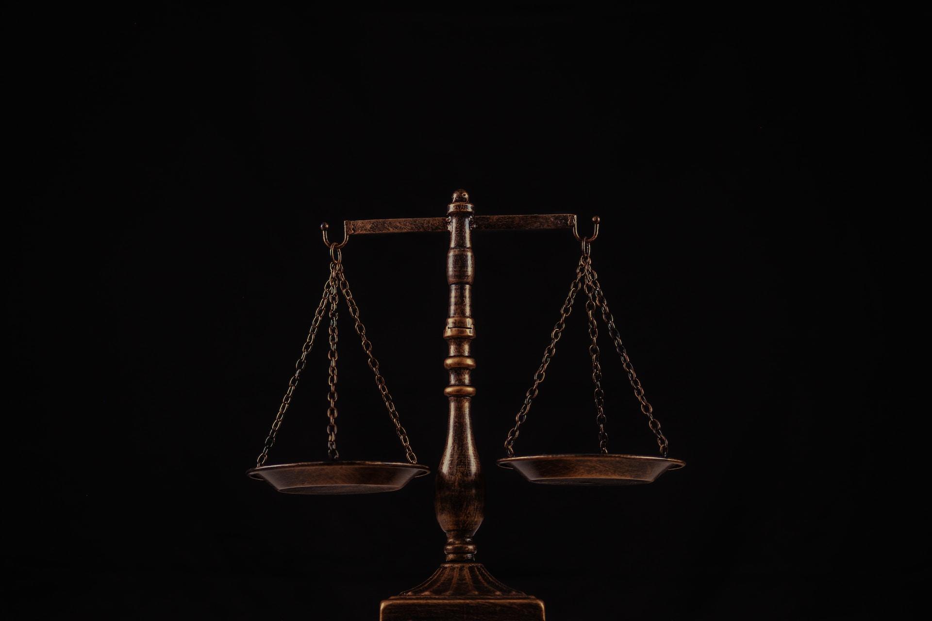 Zwei Waagschalen sind mit Ketten an Haken an einem Balken gehängt.