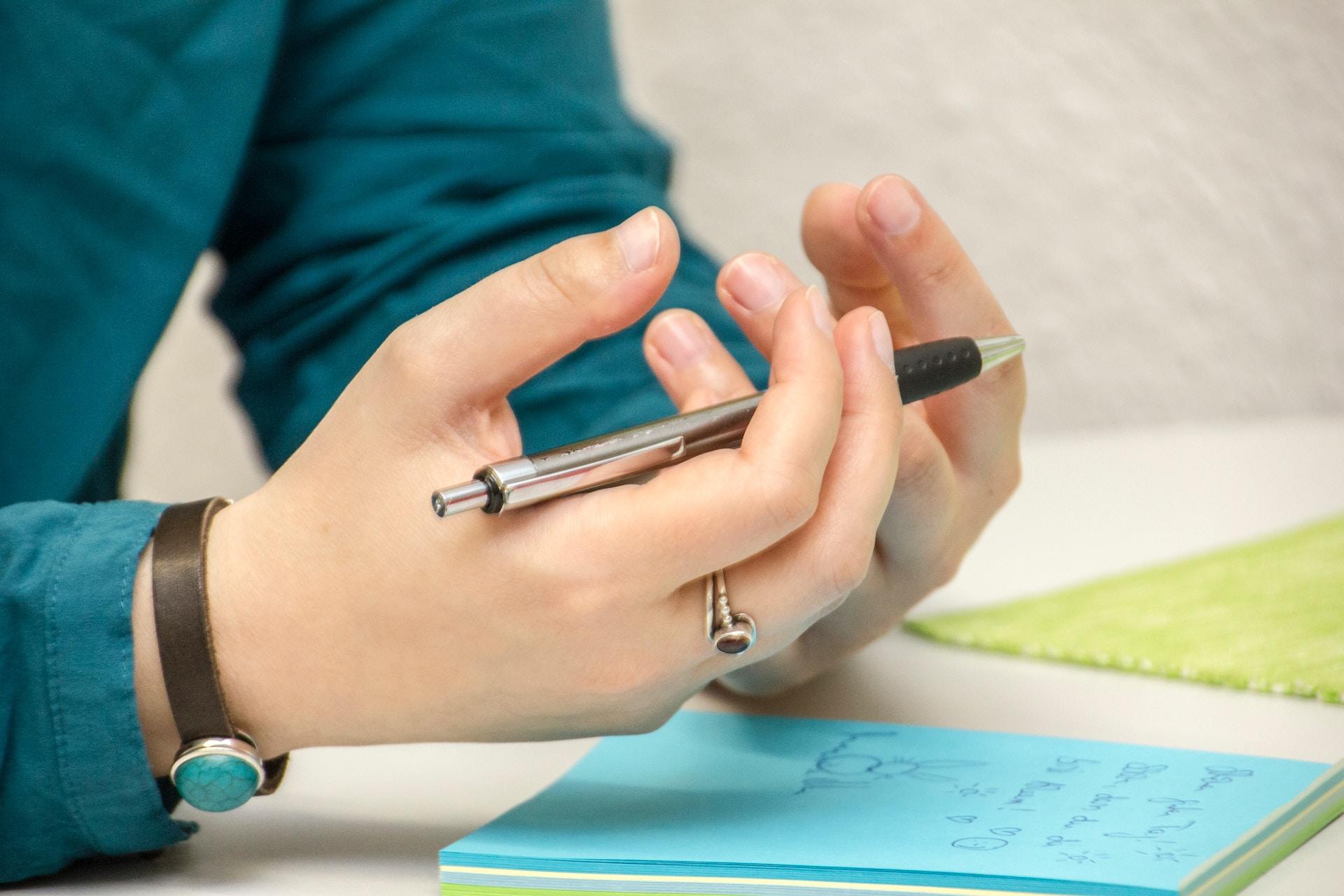 Zwei Hände mit Stift in der Hand und Block vor sich.
