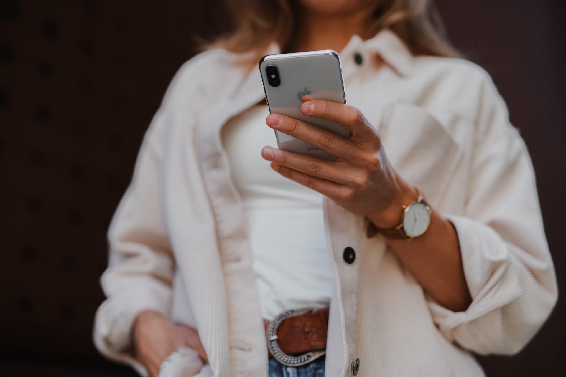 Eine weiß angezogene Person hält ein Smartphone in einer Hand vor ihrem Körper.