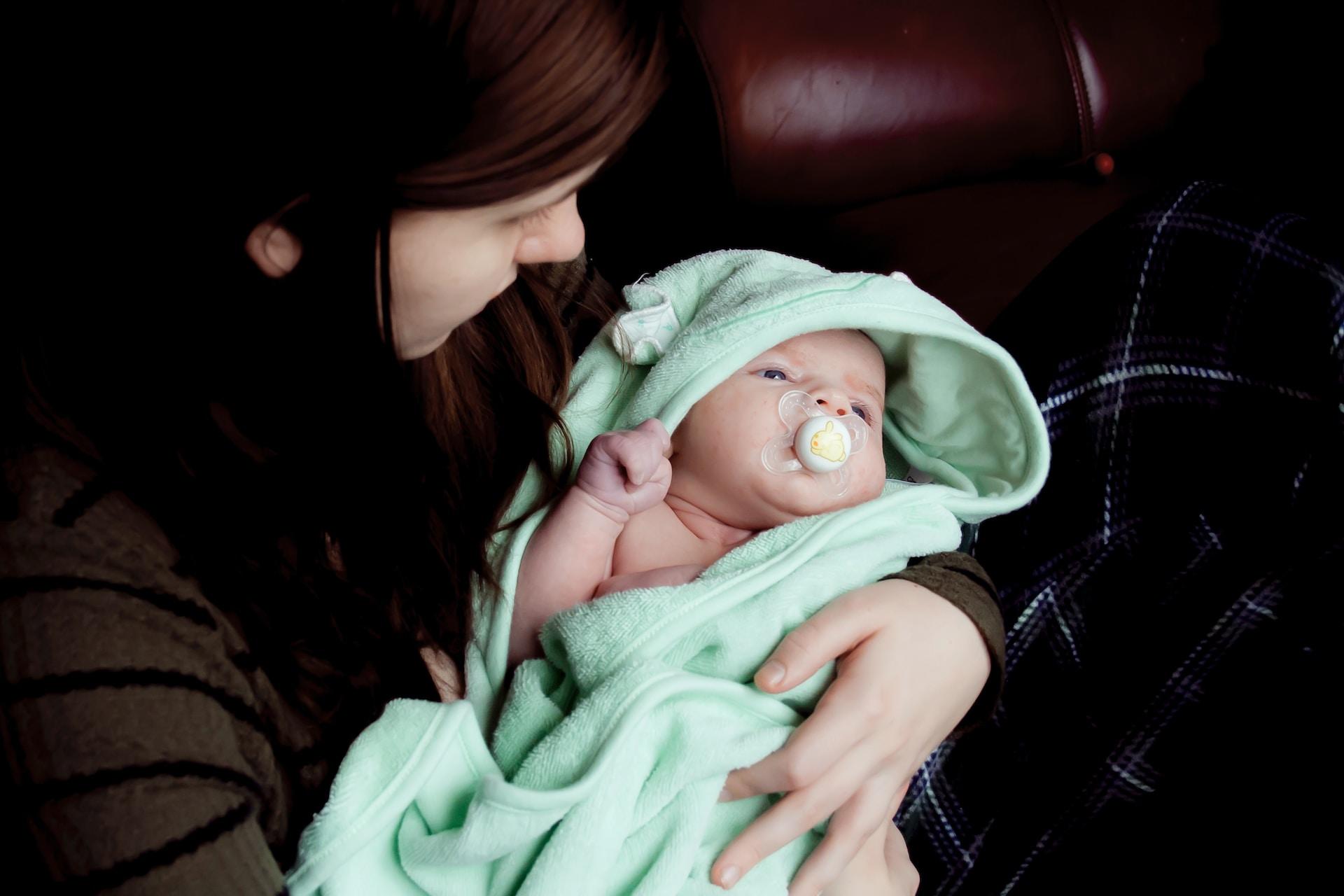 Eine erwachsene Person hält ein in ein Handtuch eingewickeltes Baby im Arm.