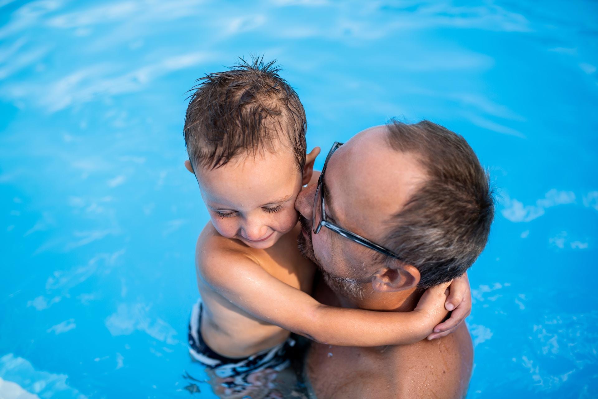 Eine erwachsene Person hält ein kleines Kind im Wasser auf den Armen.