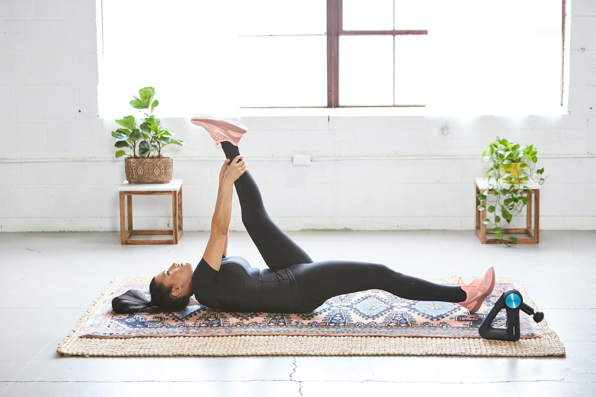 Frau liegt in einem Yogastudio auf Matte und strecht ihr linkes Bein für mehr Beweglichkeit.