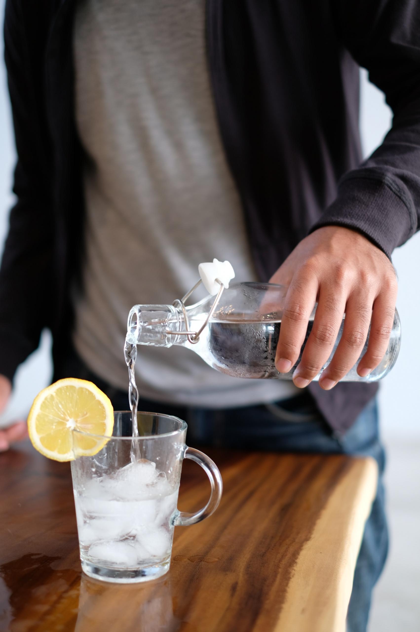 Viel Trinken wie dieses Glas Wasser von einem jungen Mann auf einem Tisch eingeschenkt befördert einen flachen Bauch.