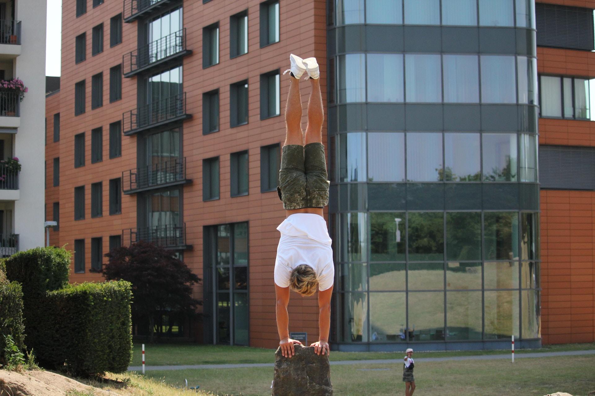 Mann in weißem Shirt macht Handstand auf Stein.