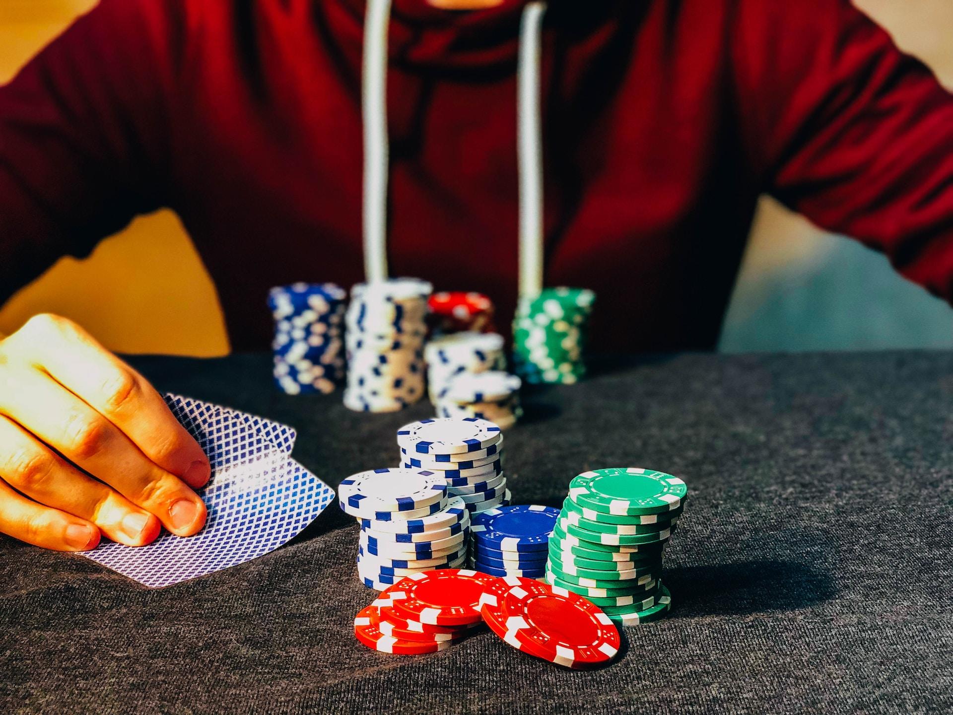 Person in rotem Pulli hält Spielkarten in der Hand und hat Pokerchips vor sich.