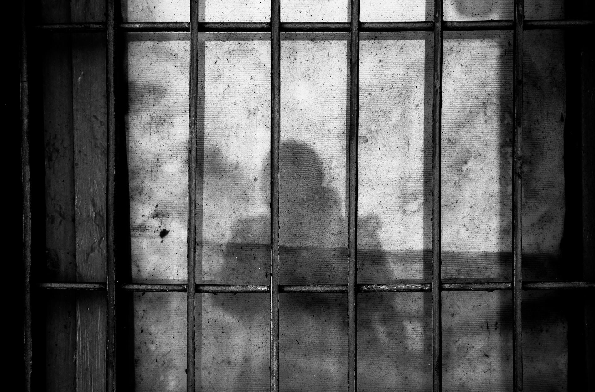 Schatten einer Person an der Wand hinter Gittern.