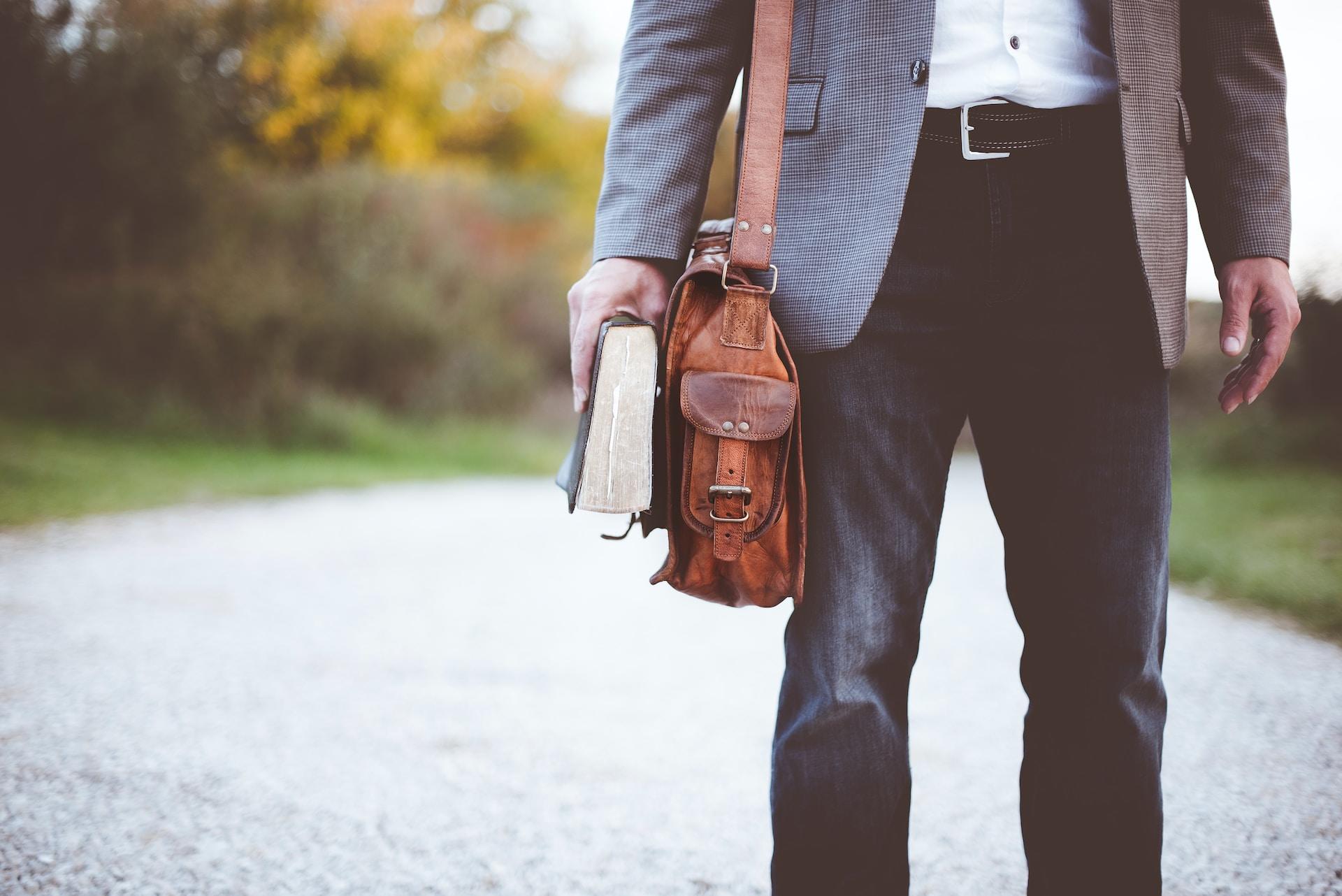 Mann mit Umhängetasche und Buch in der Hand.