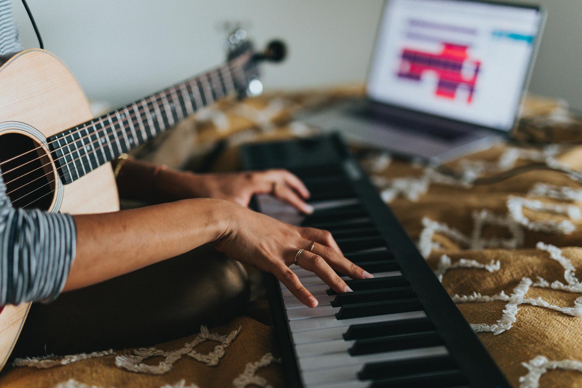 Hände einer am Keyboard sitzende Frau mit Giarre auf den Beiden und Music Programm am Laptop.