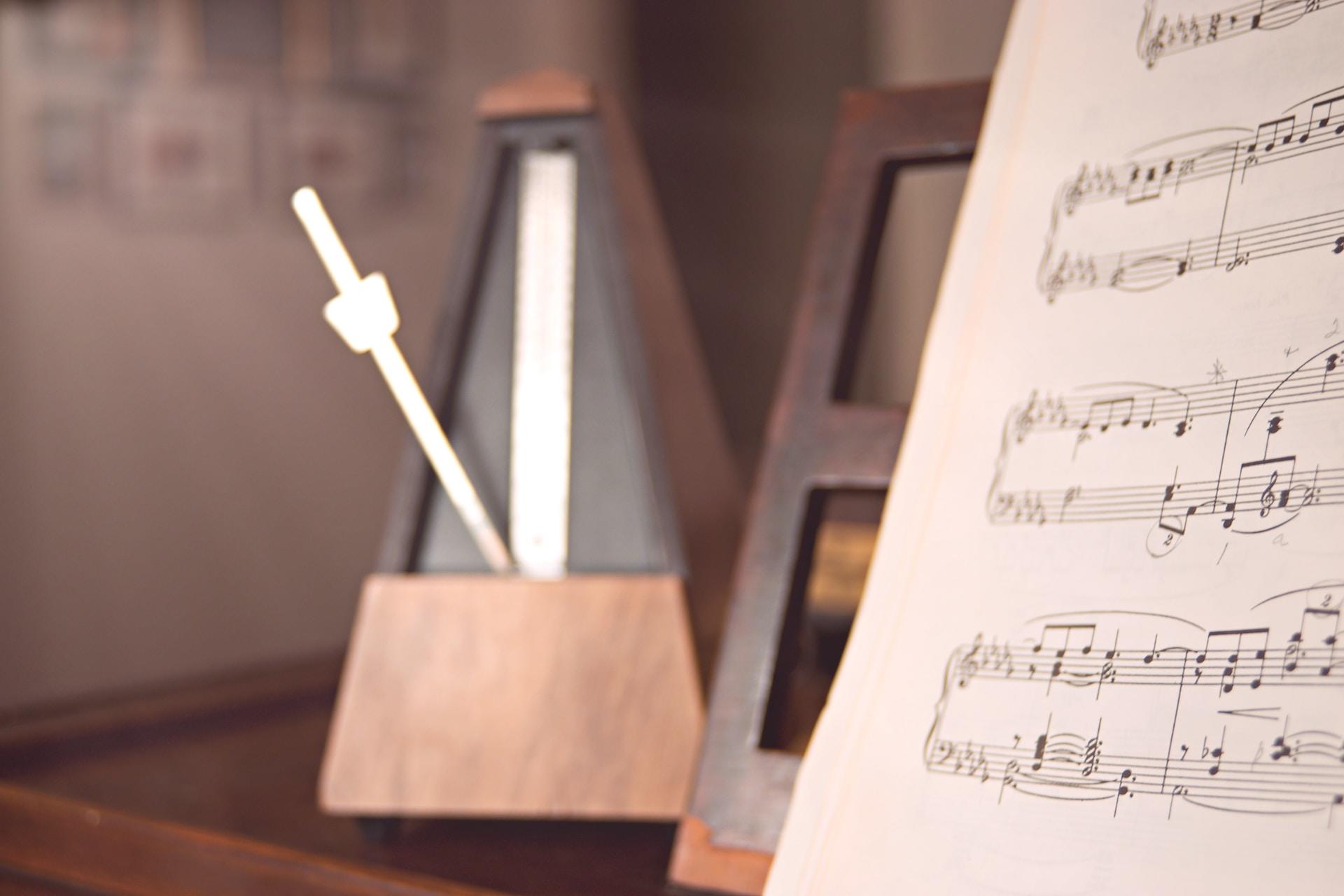 Notenblatt auf Klavierständer mit Metronom daneben sind Hilfsmittel für den Musikunterricht.