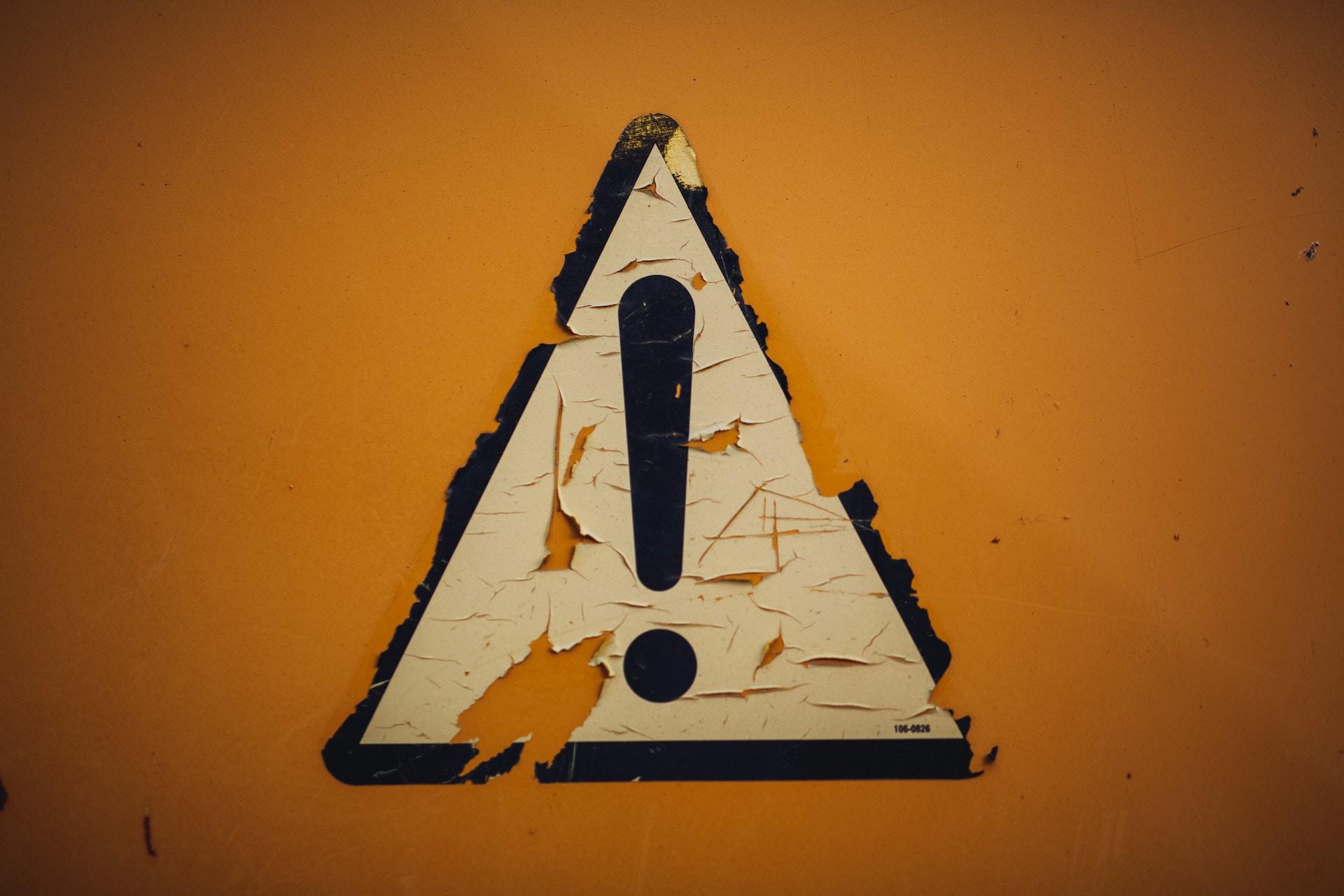 Ein kaputtes Achtung-Schild vor gelbem Hintergrund
