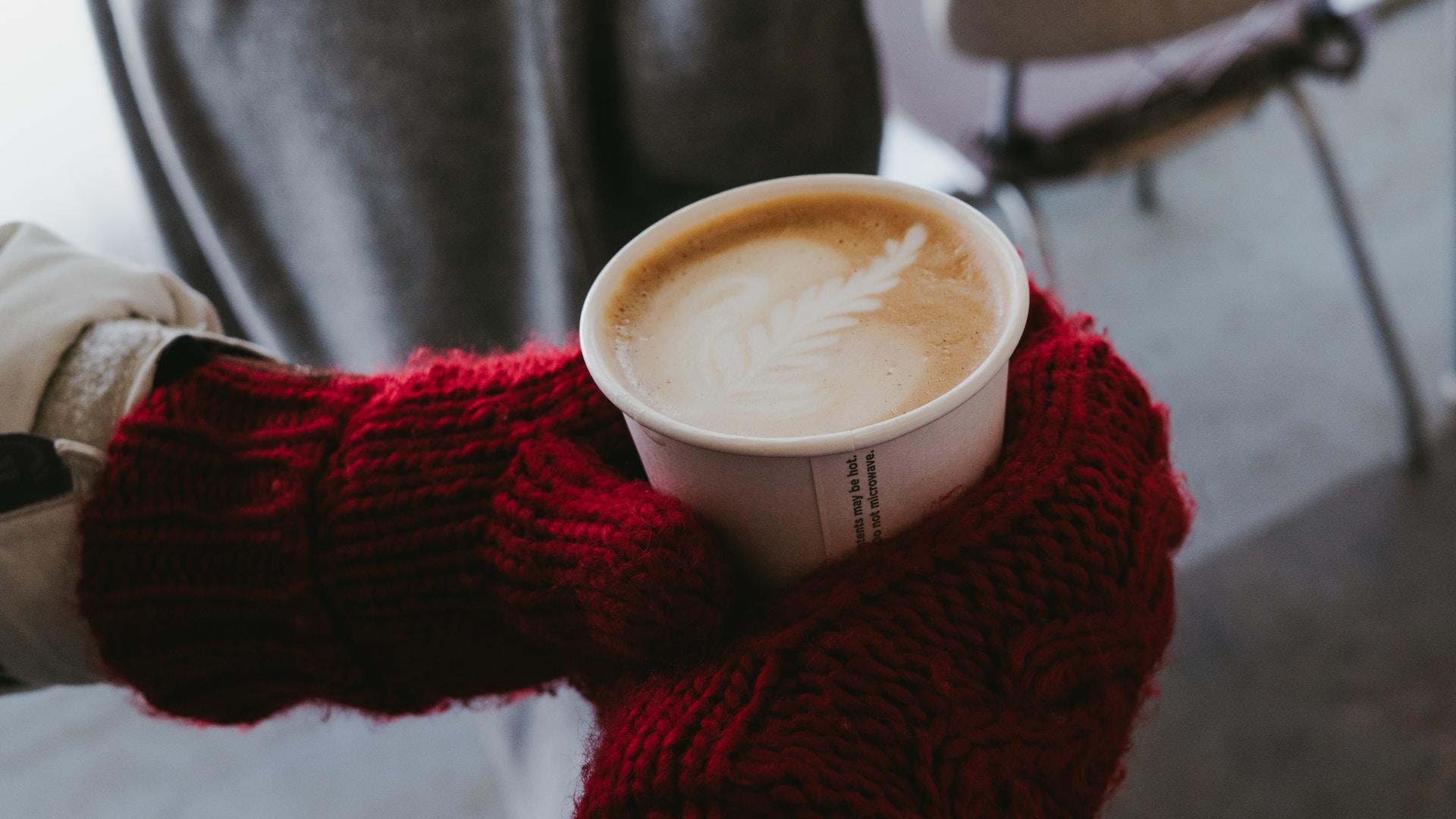 Zwei Hände mit roten Handschuhen halten Kaffeebecher fest.