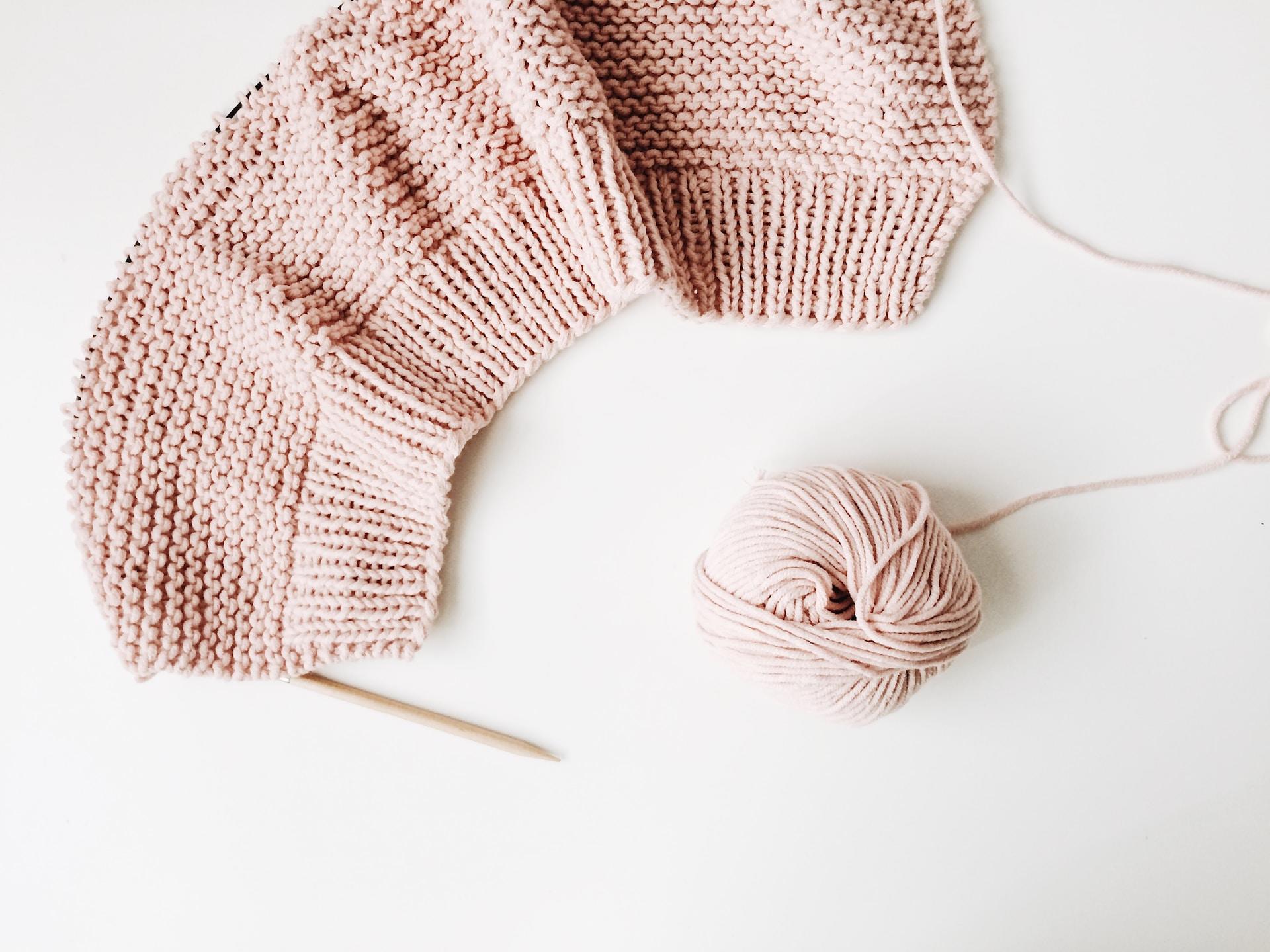 Strickmuster mit rosa Wolle auf weißer Unterlage.