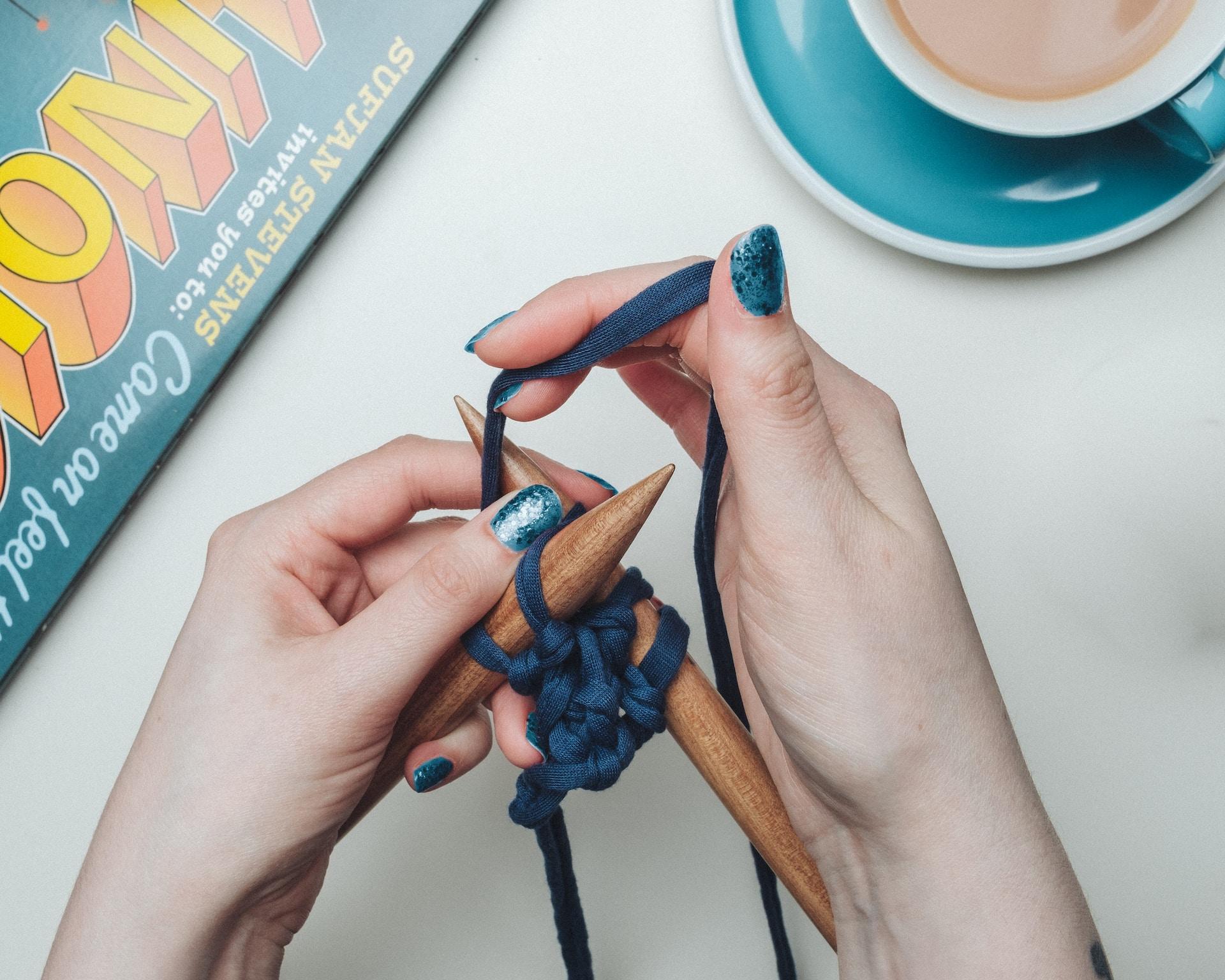 Zwei Hände mit Stricknadeln aus Hinz und blauem Garn.