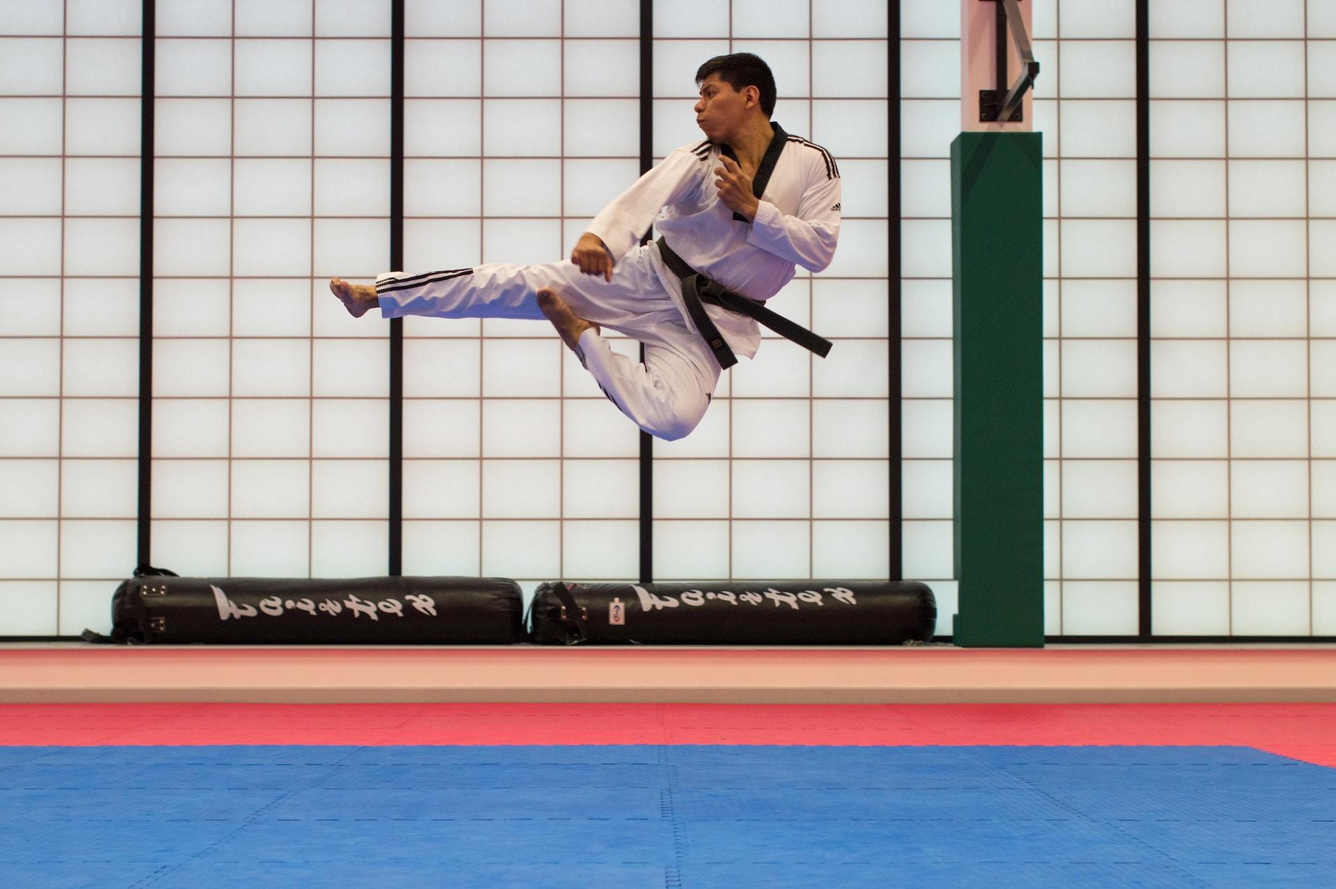 Mann in Karate Anzug Springt über Matte.