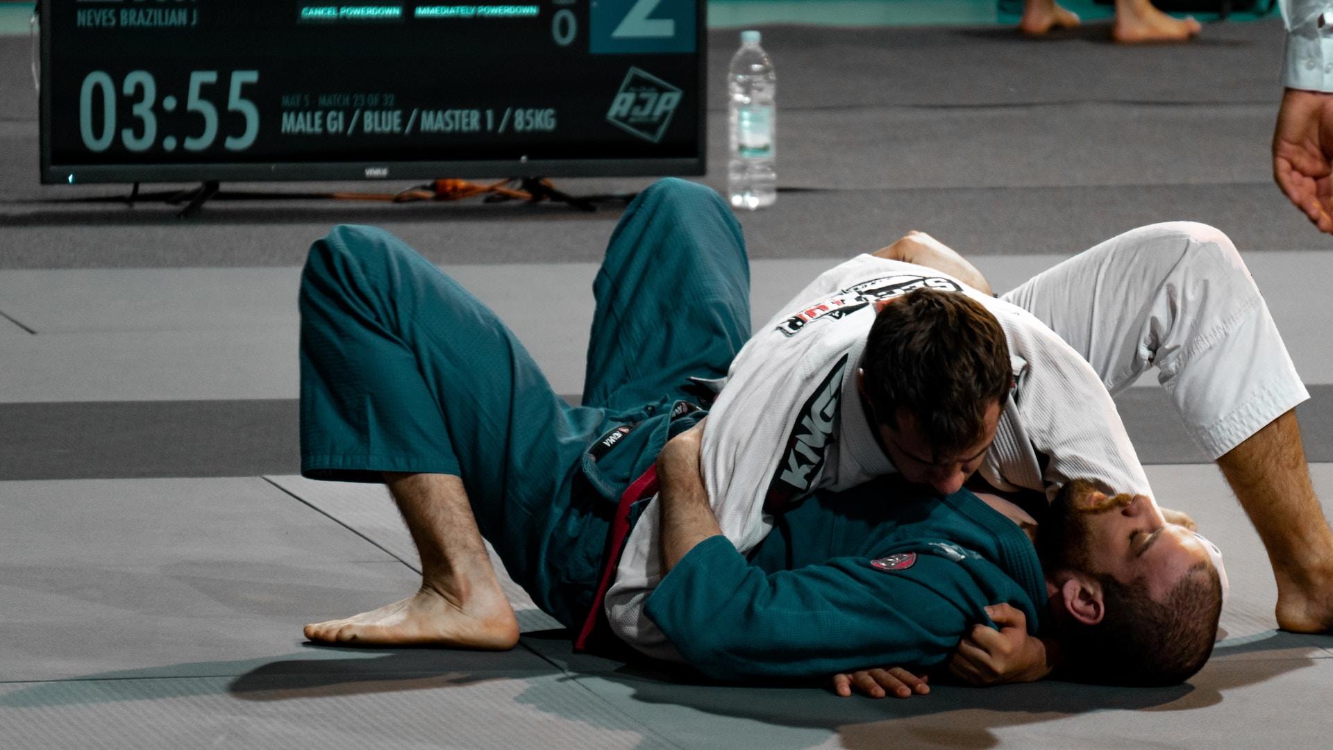 Zwei Männer in Judo Klamotten ringen auf einer Matte.