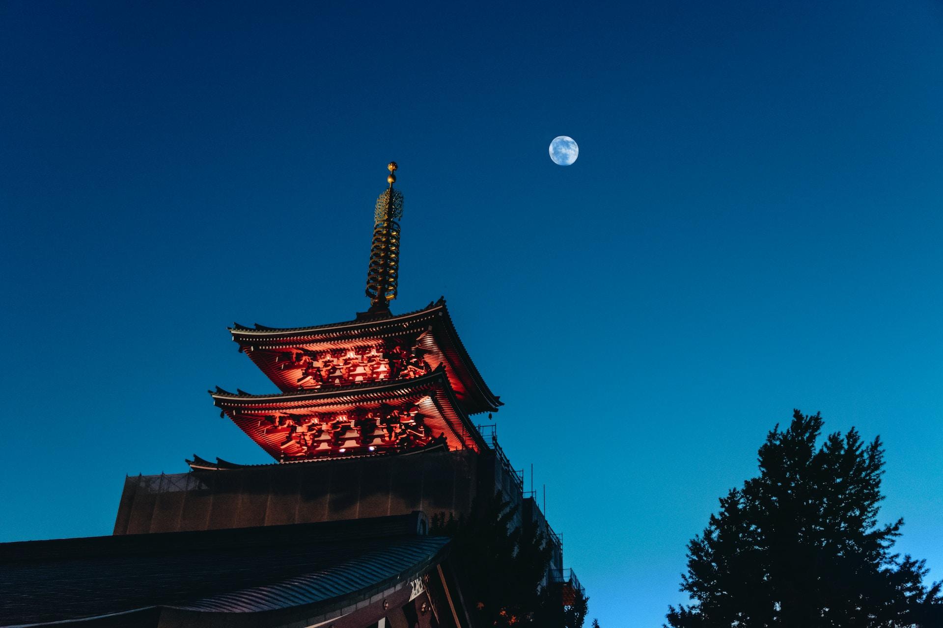 Japanischer Tempel vor Mond und dunklem Himmel.