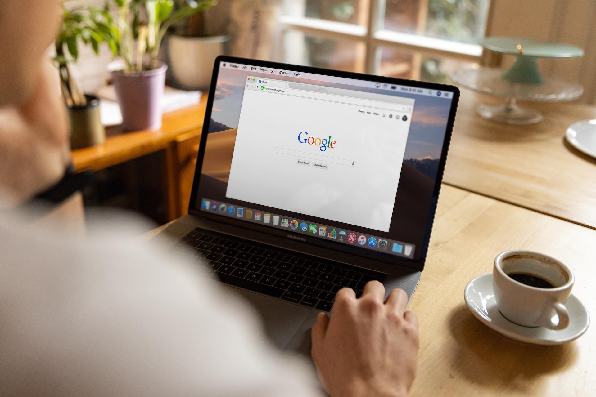 Aufgeklappter Laptop mit Google Suchmaschine und Kaffeetasse nebendran.