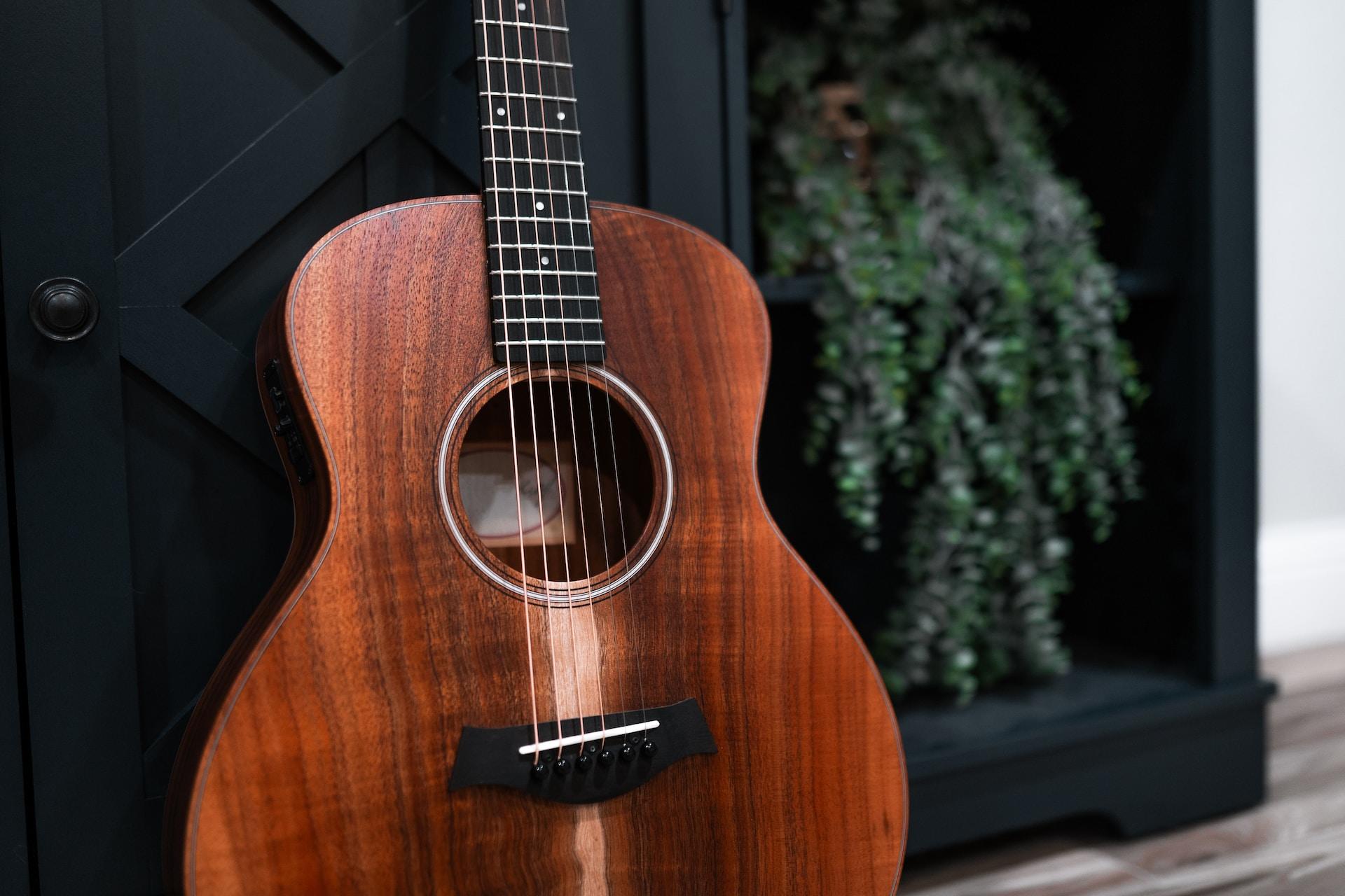 Eine dunkelbraune Akustikgitarre an eine Wand gelehnt