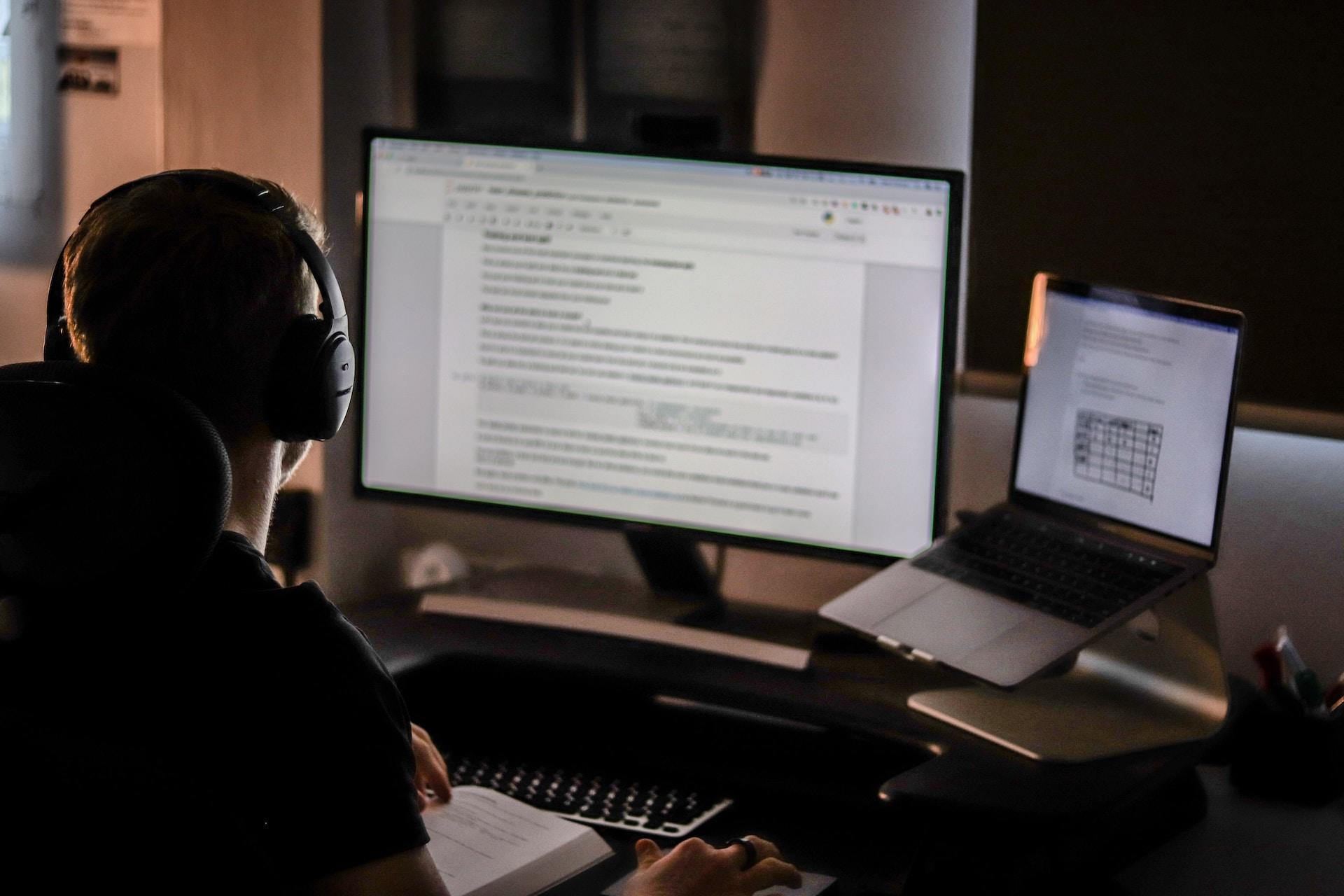 Mann mit Kopfhörern sitzt vor großem Computerbildschirm.