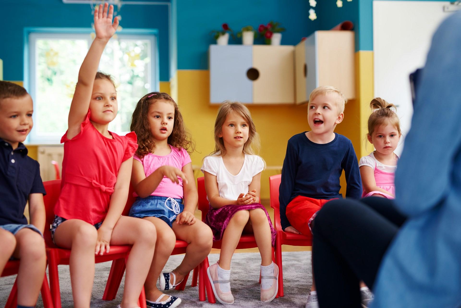 Mehrere Kinder sitzen nebeneinander und eines streckt die Hand auf