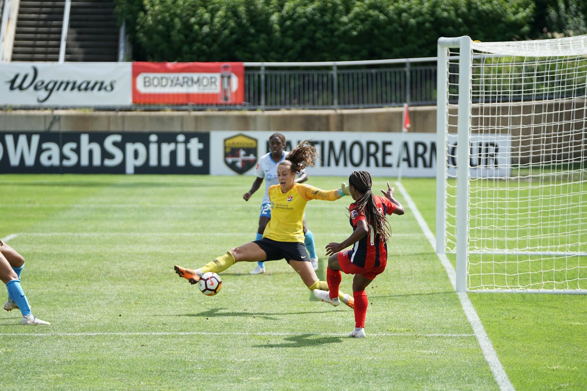 Fussballspiel mit drei Frauen und Torhüterin am Ball.