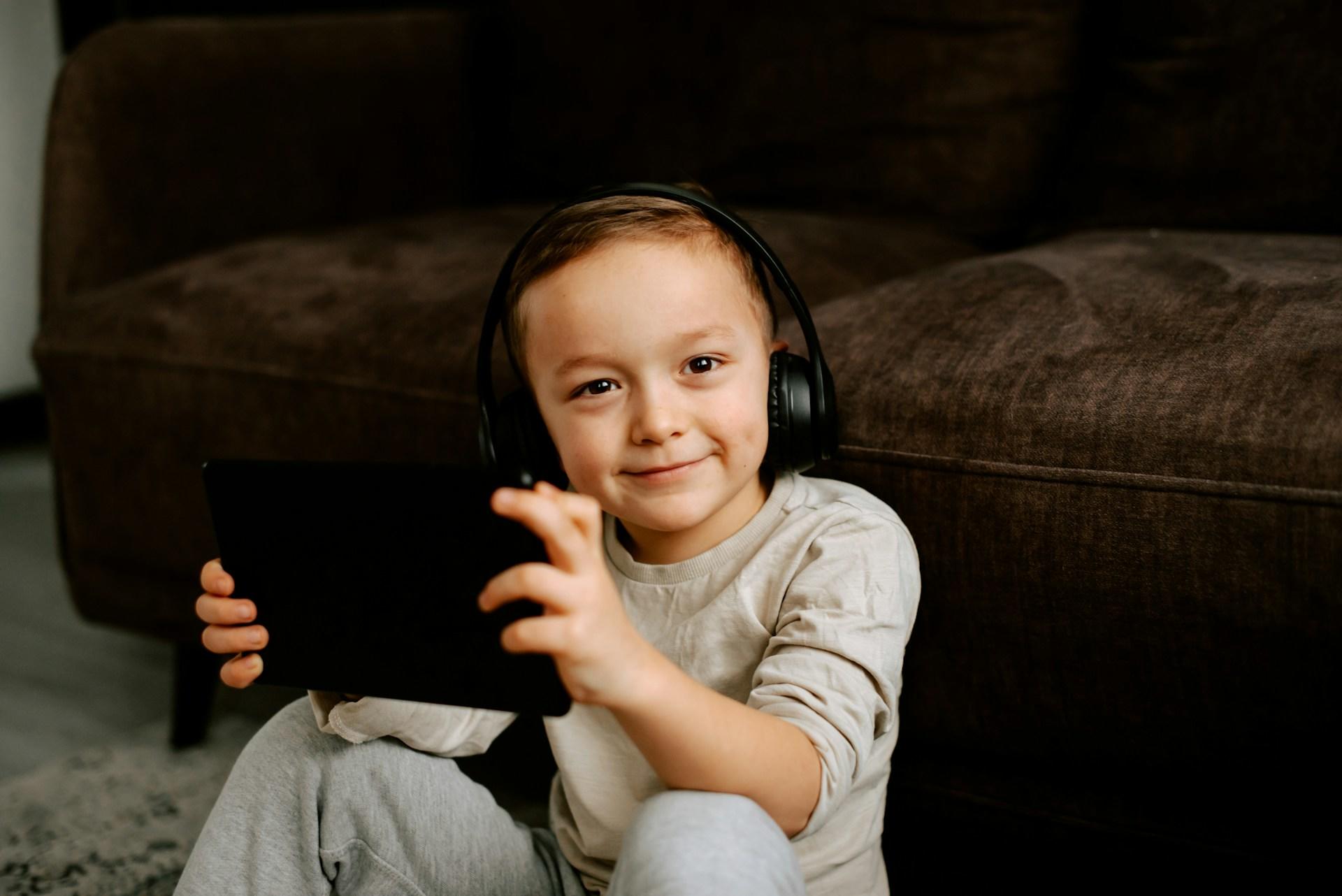 Ein Kind sitz mit Kopfhörern und einem Tablet vor einem Sofa