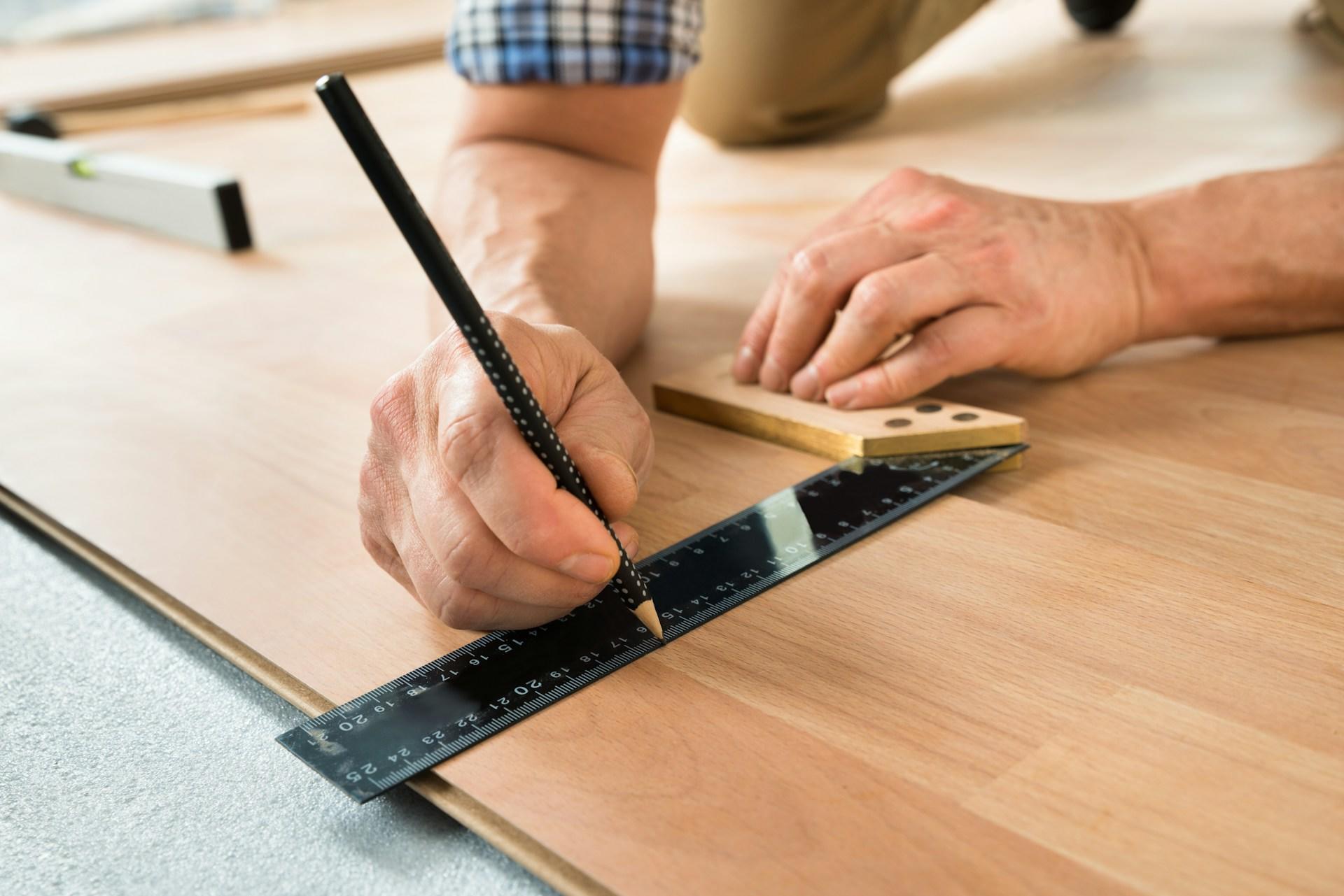 eine Person arbeitet mit Lineal und Bleistift auf einer Holzplatte