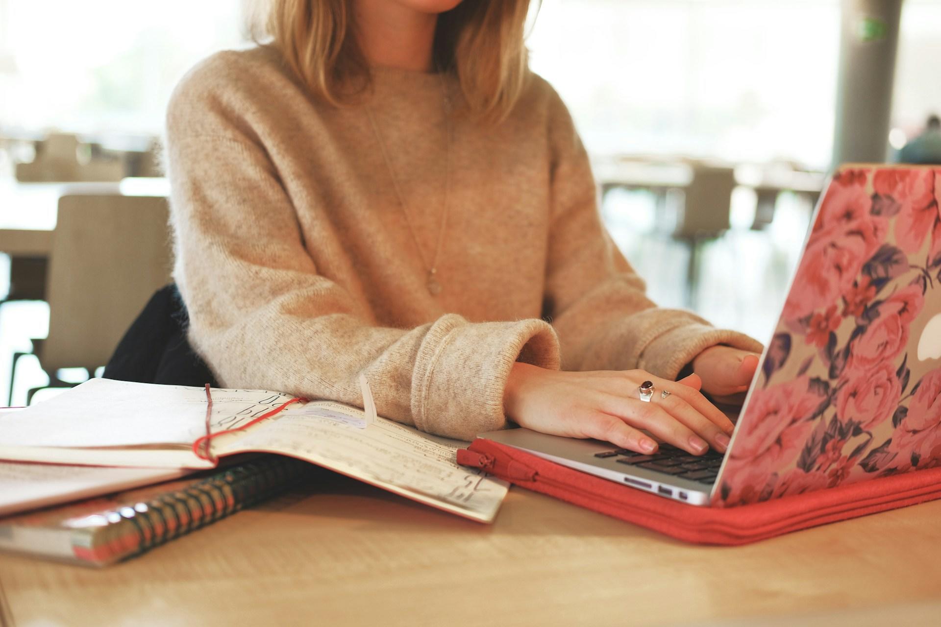 Frau sitzt an Schreibtisch und tippt etwas auf Laptop.
