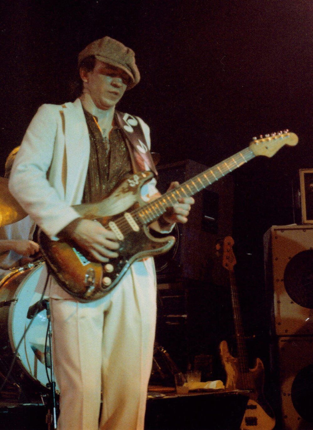 Stevie Ray Vaughan in beigem Anzug und mit Gitarre auf einer Bühne