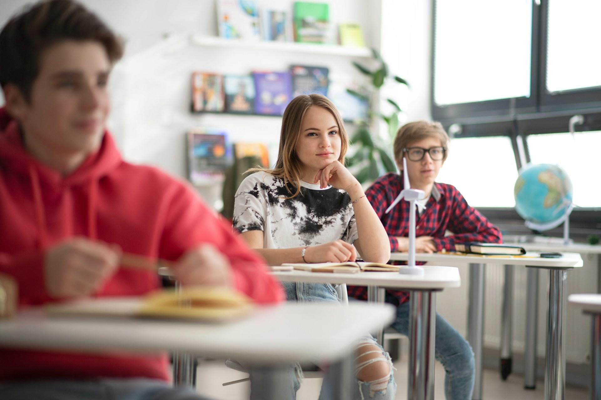 drei Kinder sitzen an Tischen in einem Schulzimmer
