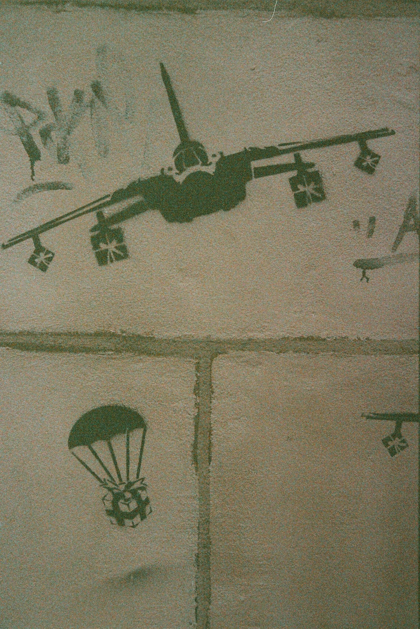 Ein Grafitti von einem Militärflugzeug, das Geschenke abwirft (Rosinenbomber)