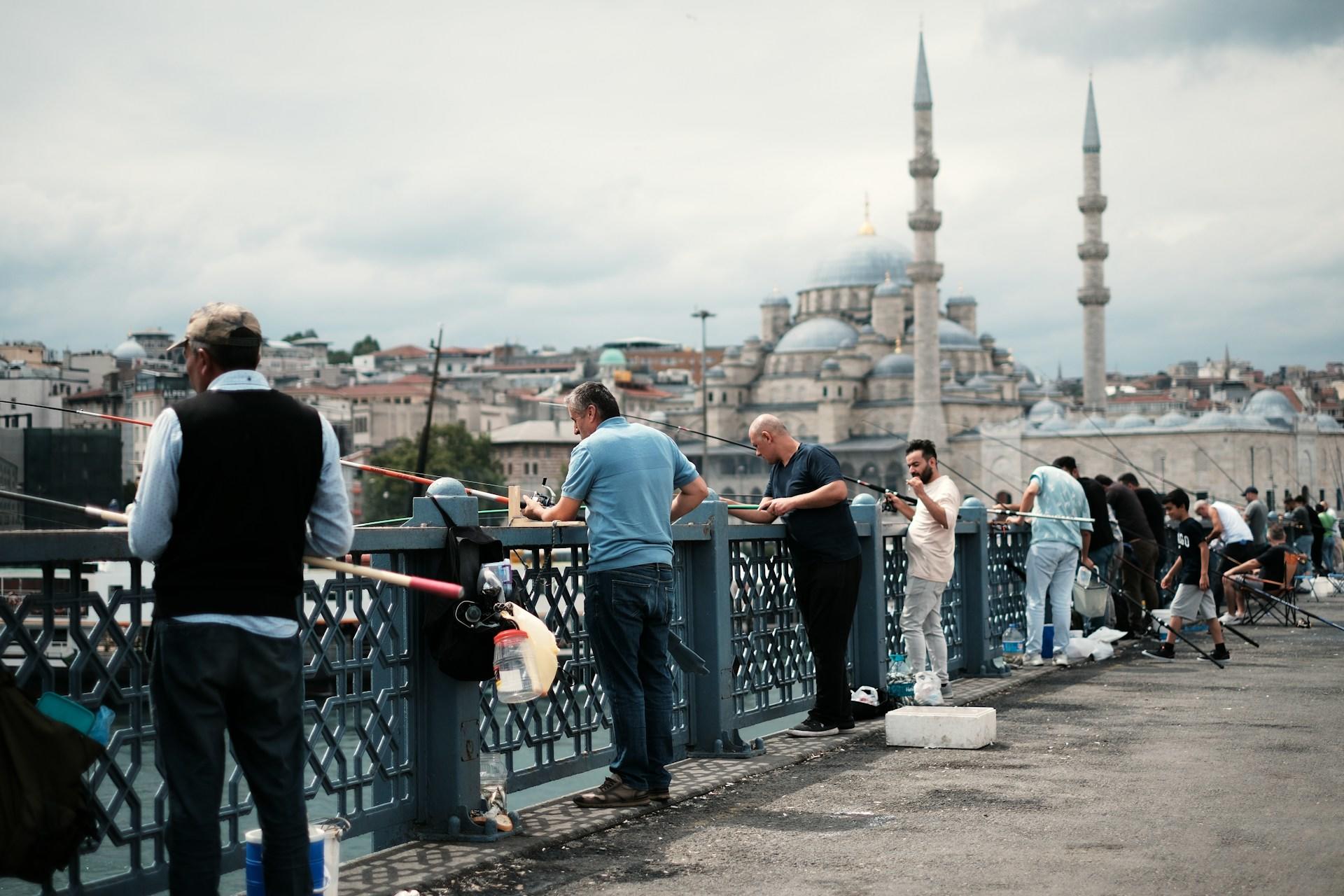 Fischer auf einer Brücke und im Hintergrund eine Moschee