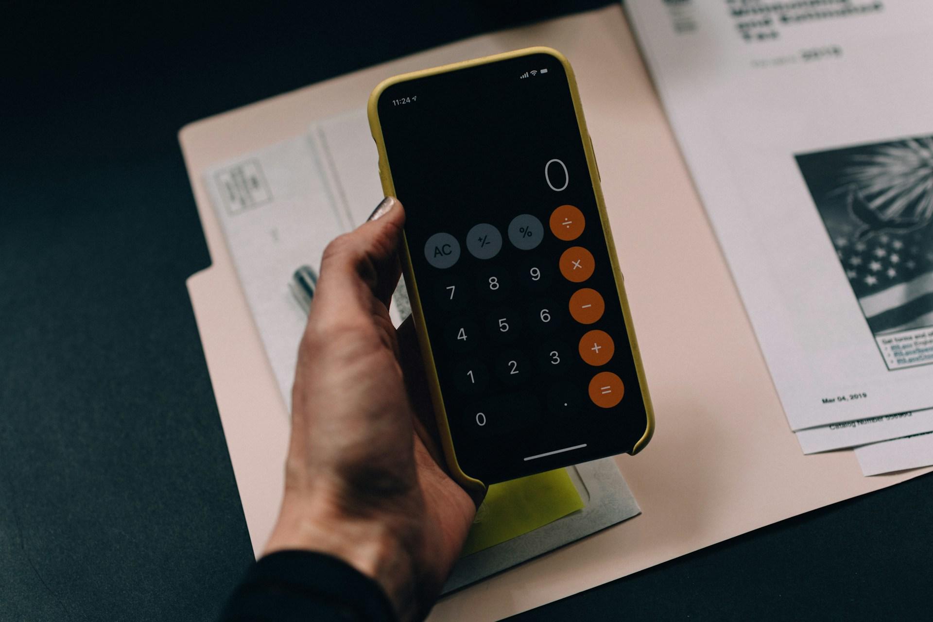 Hand hält Handy mit Taschenrechner drauf.