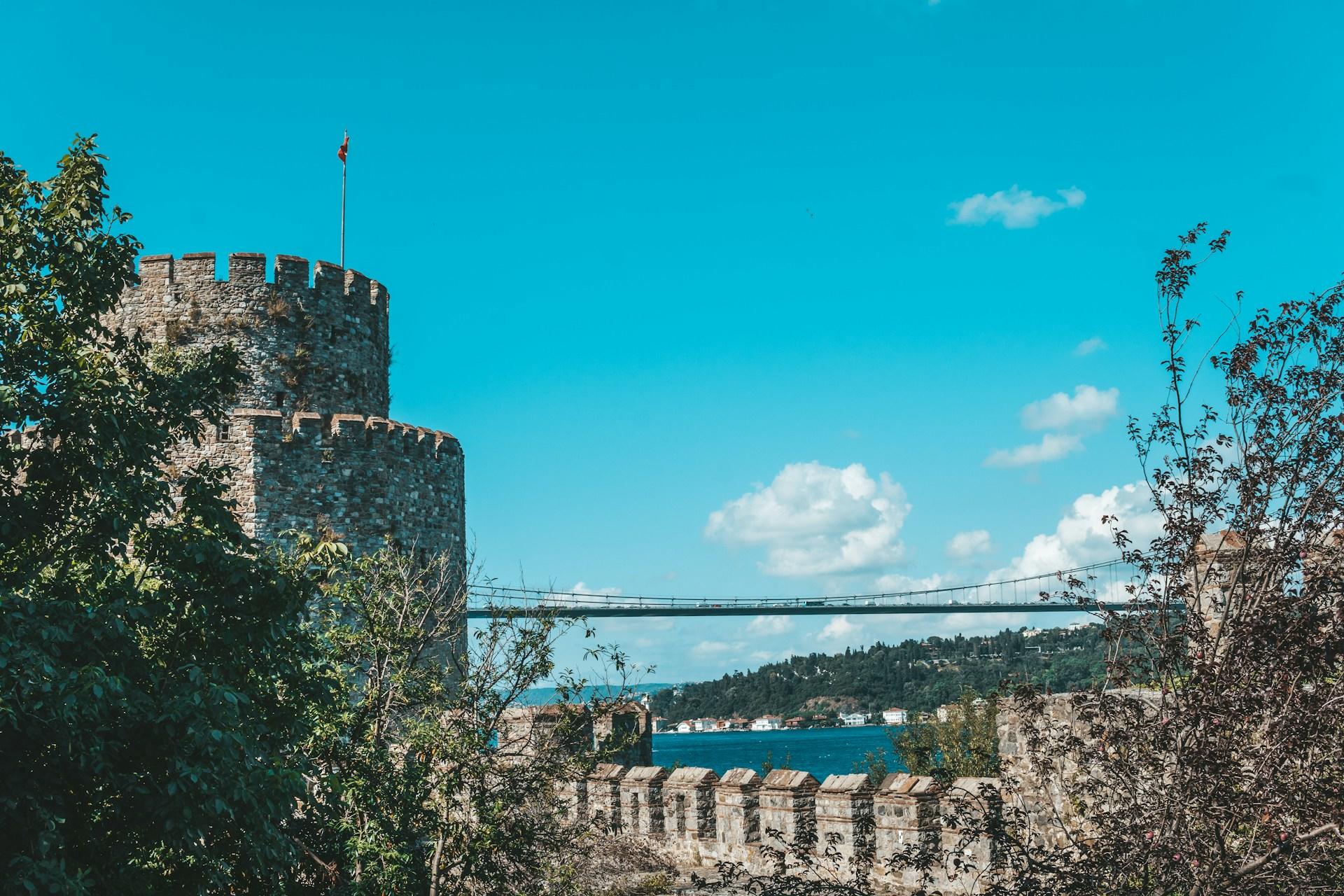 Festungsmauern mit Turm und im Hintergrund eine lange Brücke