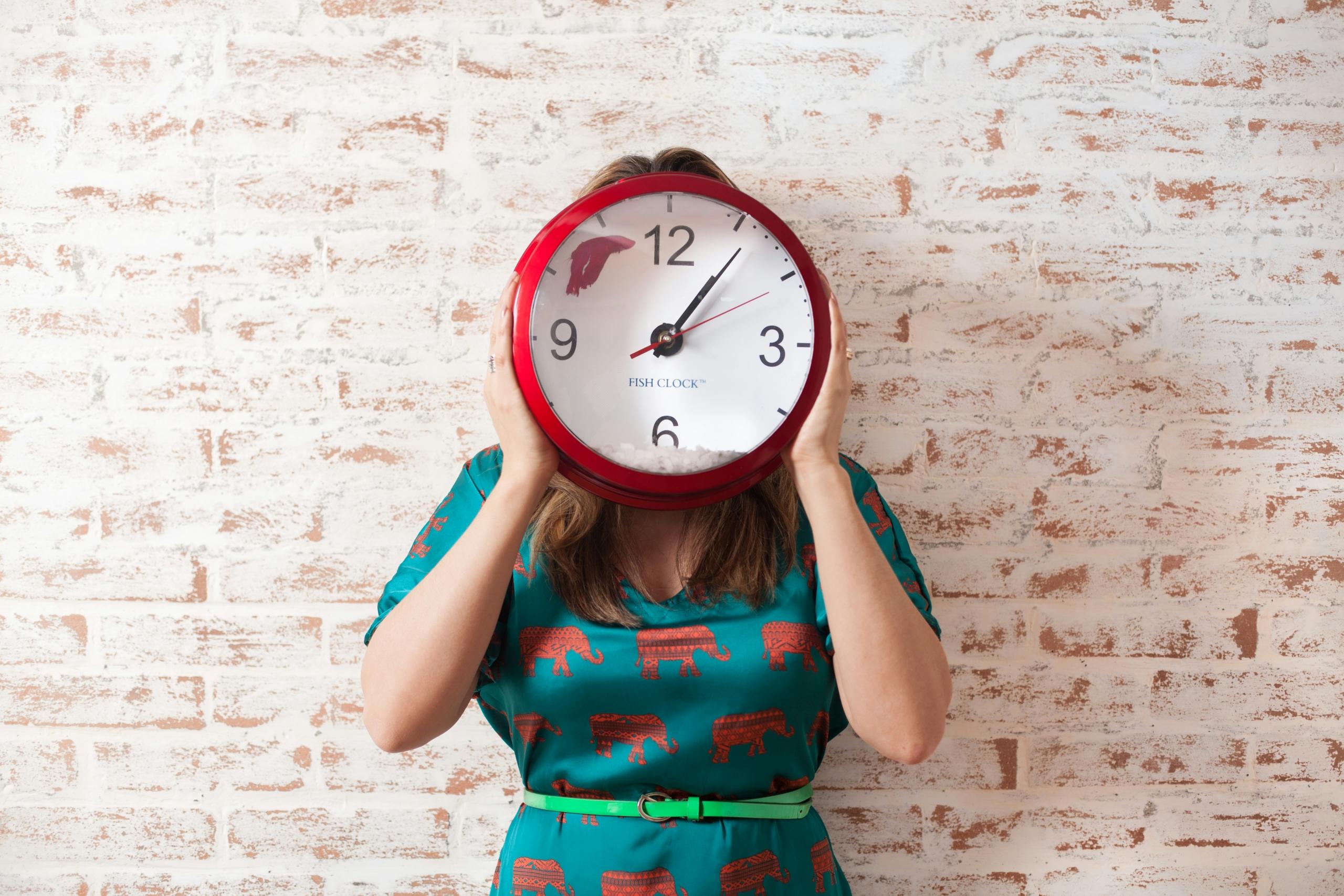 Eine Person hält eine riesige Uhr vor ihrem Gesicht