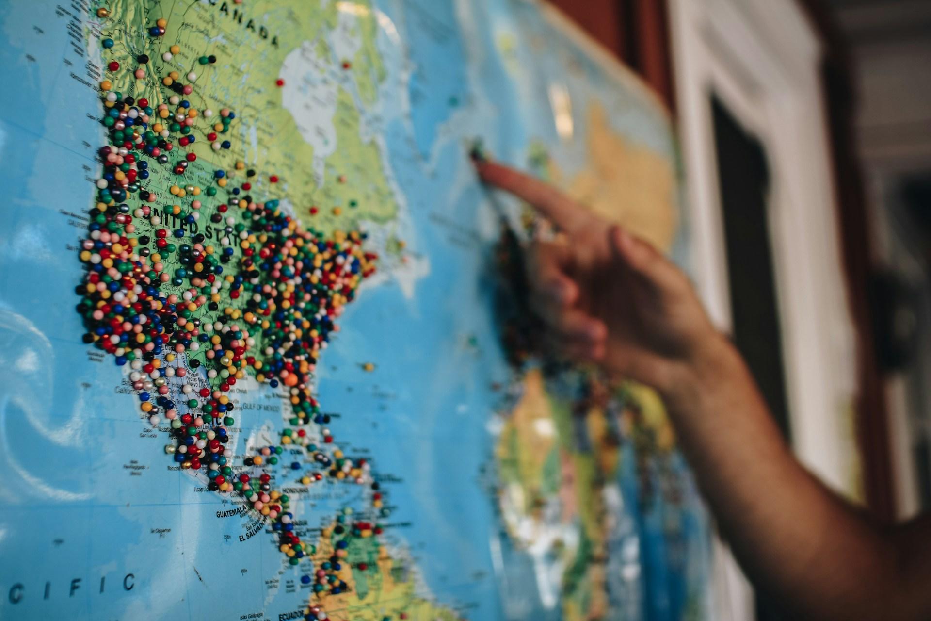 Landkarte mit Pins auf Amerika auf die eine Hand zeigt.