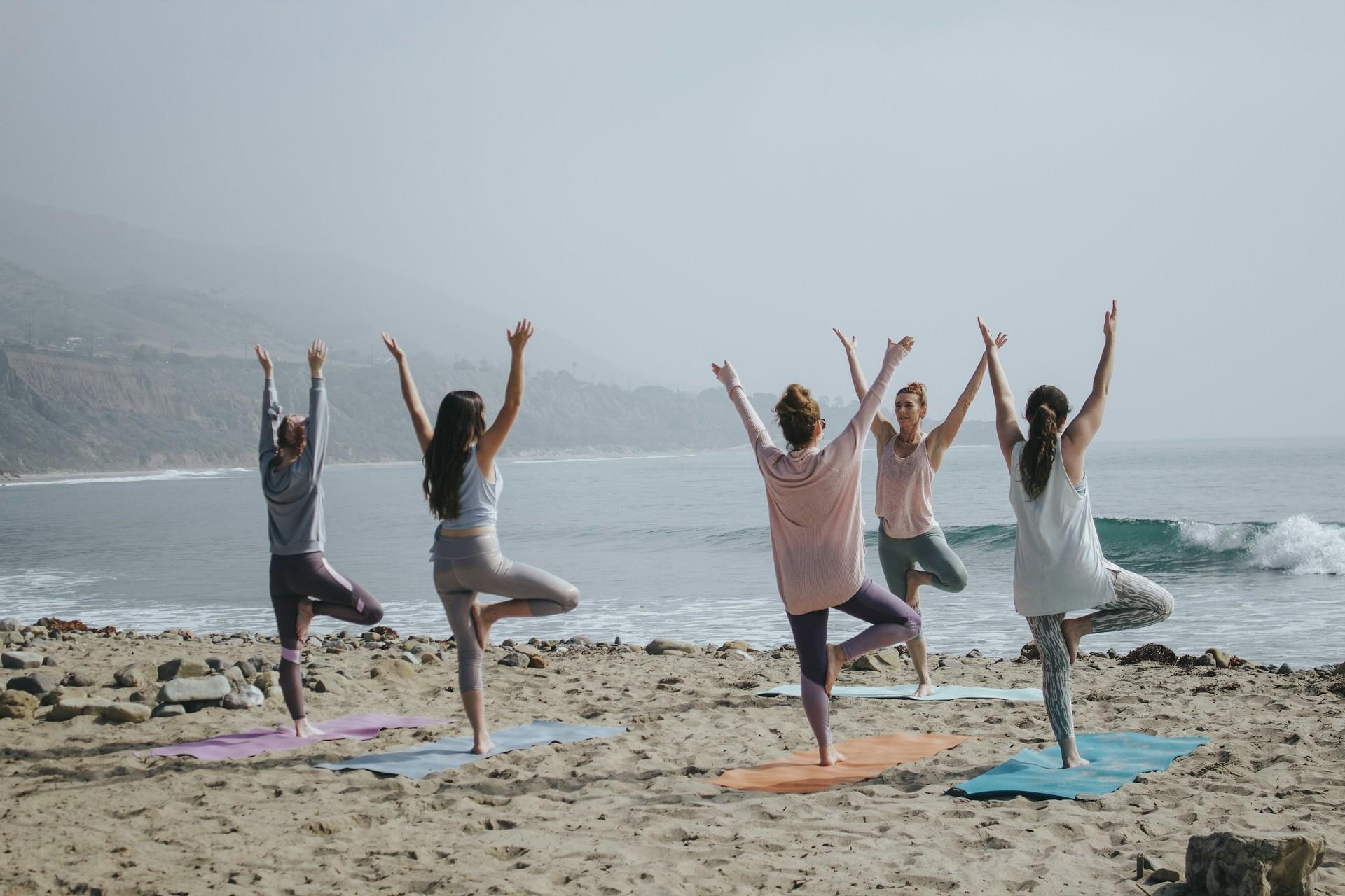 Mehrere Frauen auf Yoga Matten am Strand.