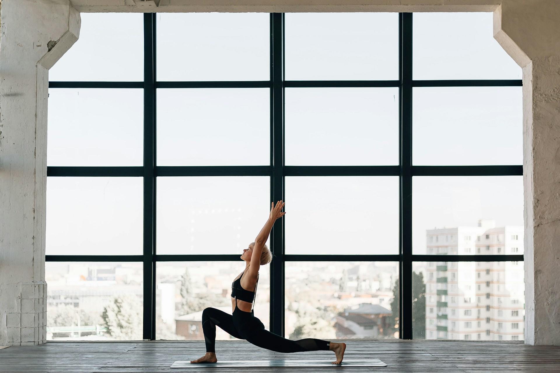 Frau in großem Raum in Yoga Position auf einer Matte.