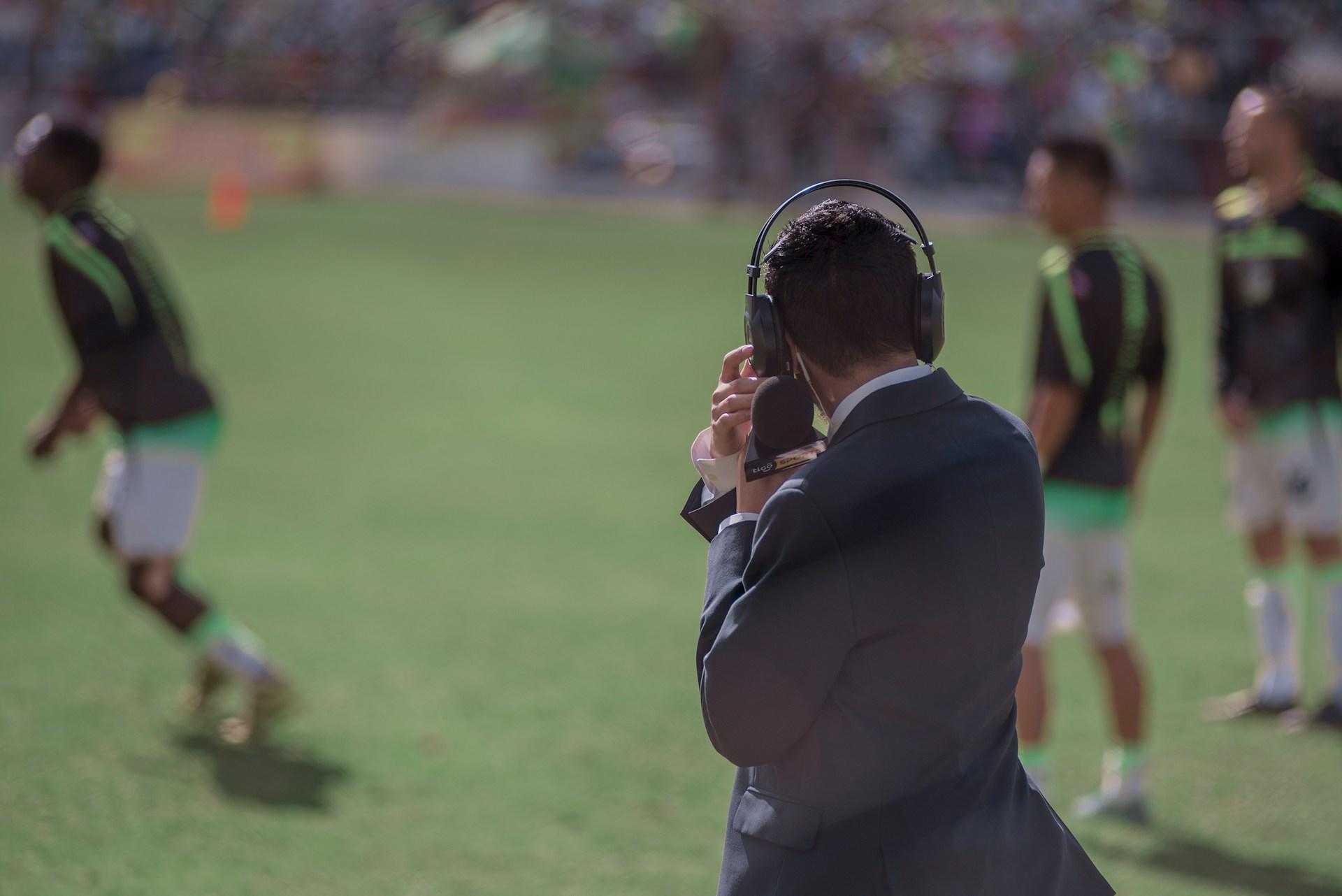 Mann mit Headset steht auf Fußballplatz.